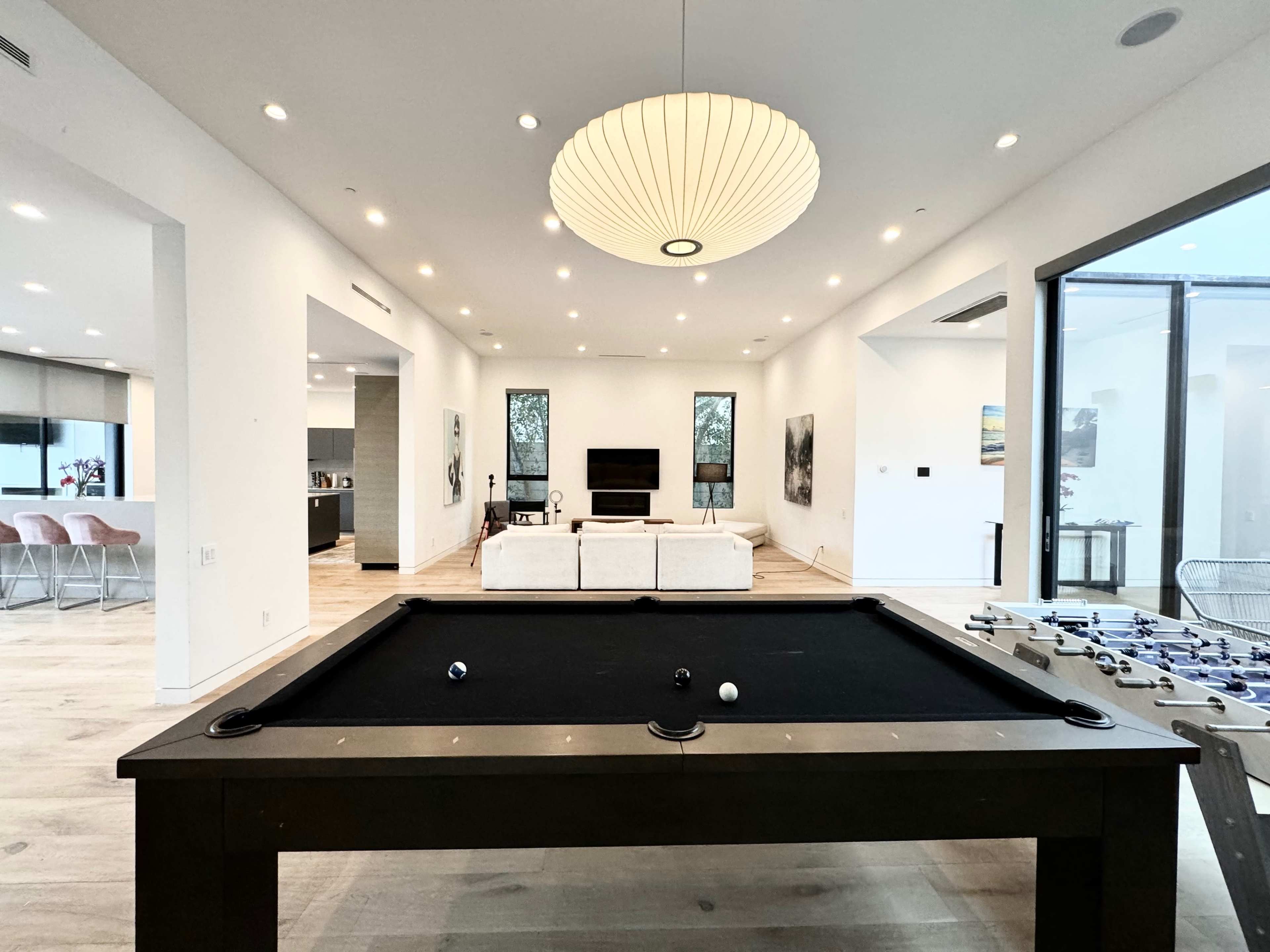 A billiard table is positioned in the foreground of a spacious room that features a living area with a sofa and a television in the background.