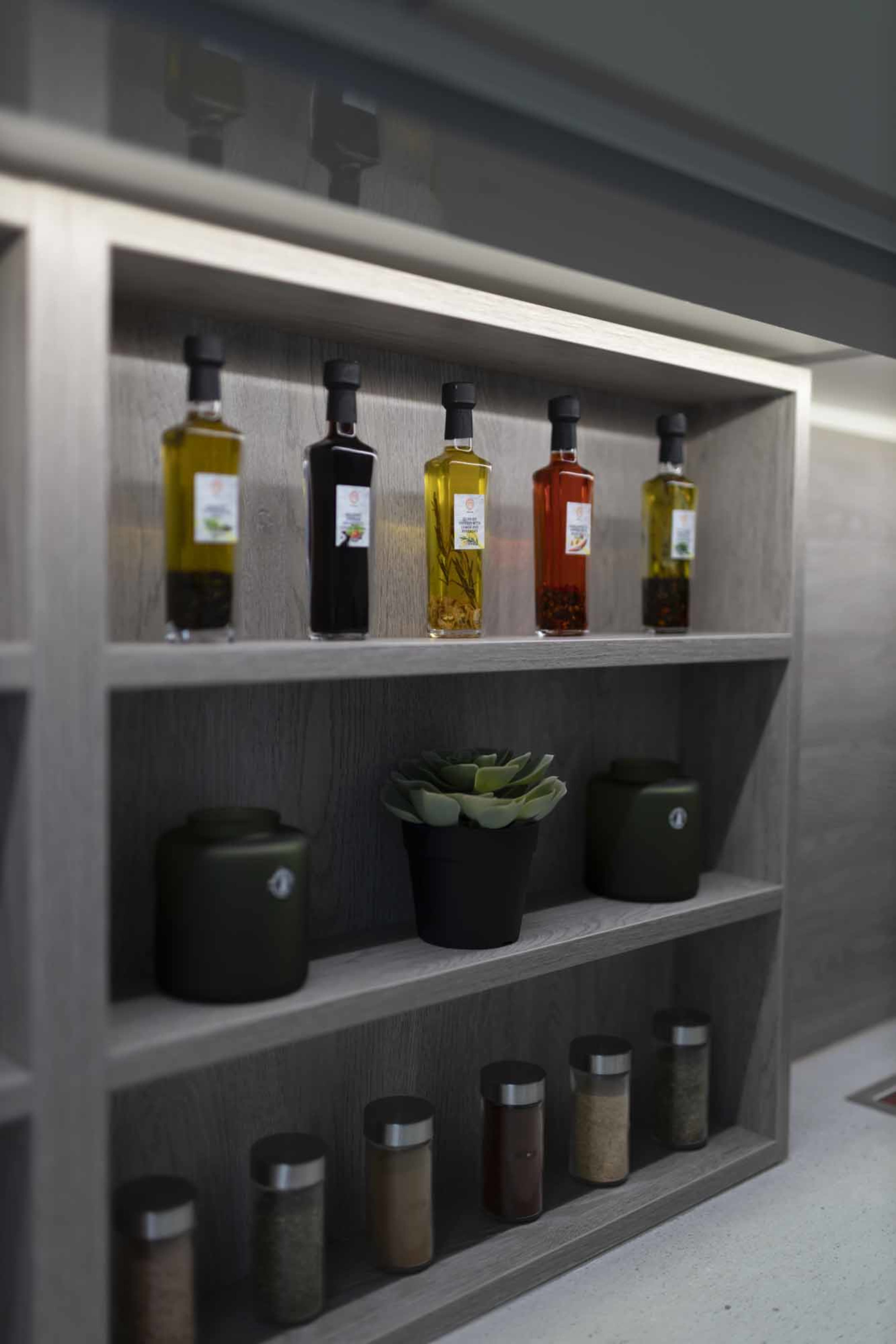 A wooden shelf displaying several bottles of oil, a potted plant, jars, and spice containers.
