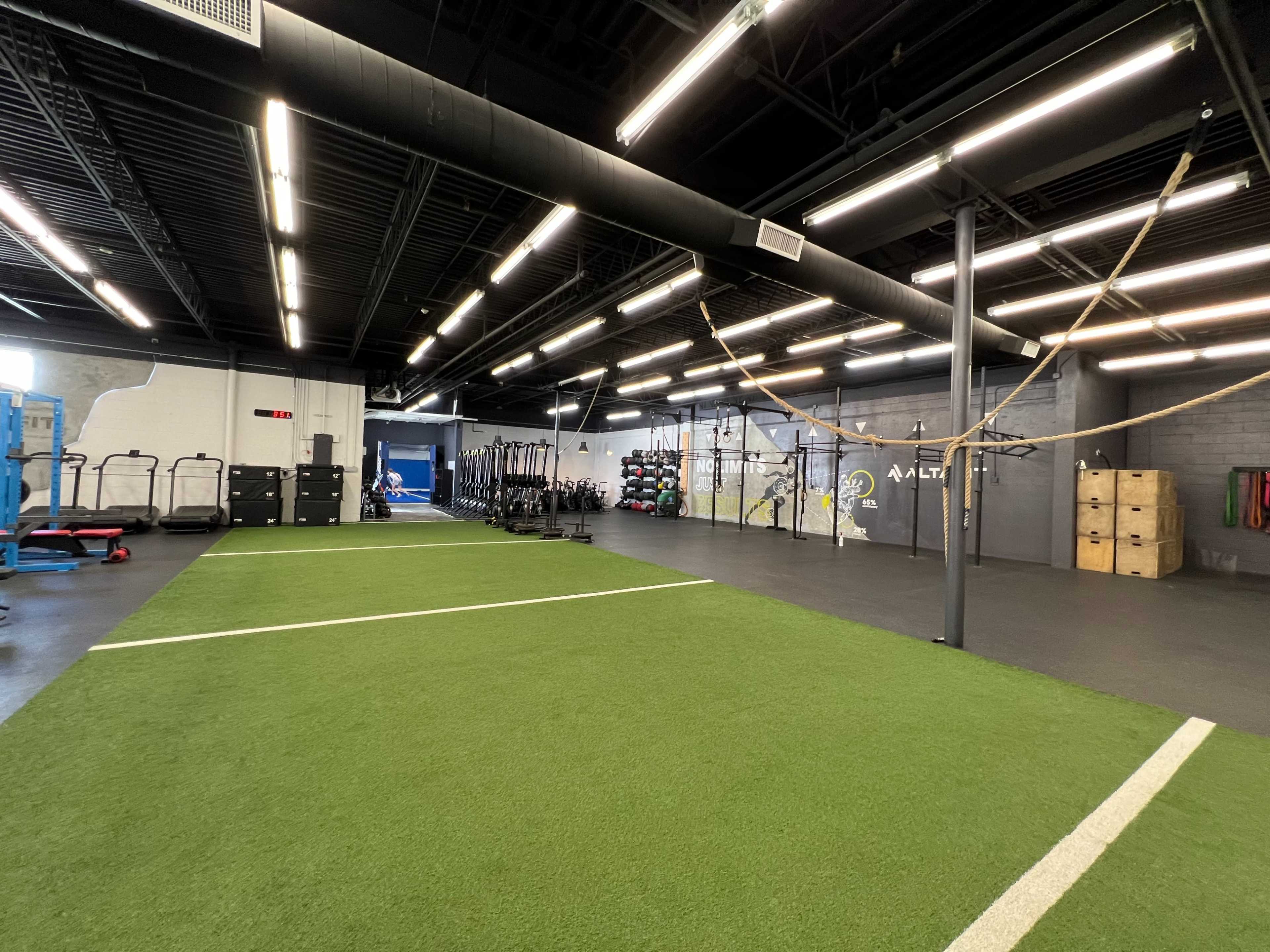 A spacious indoor gym with artificial turf, workout equipment, and storage boxes.