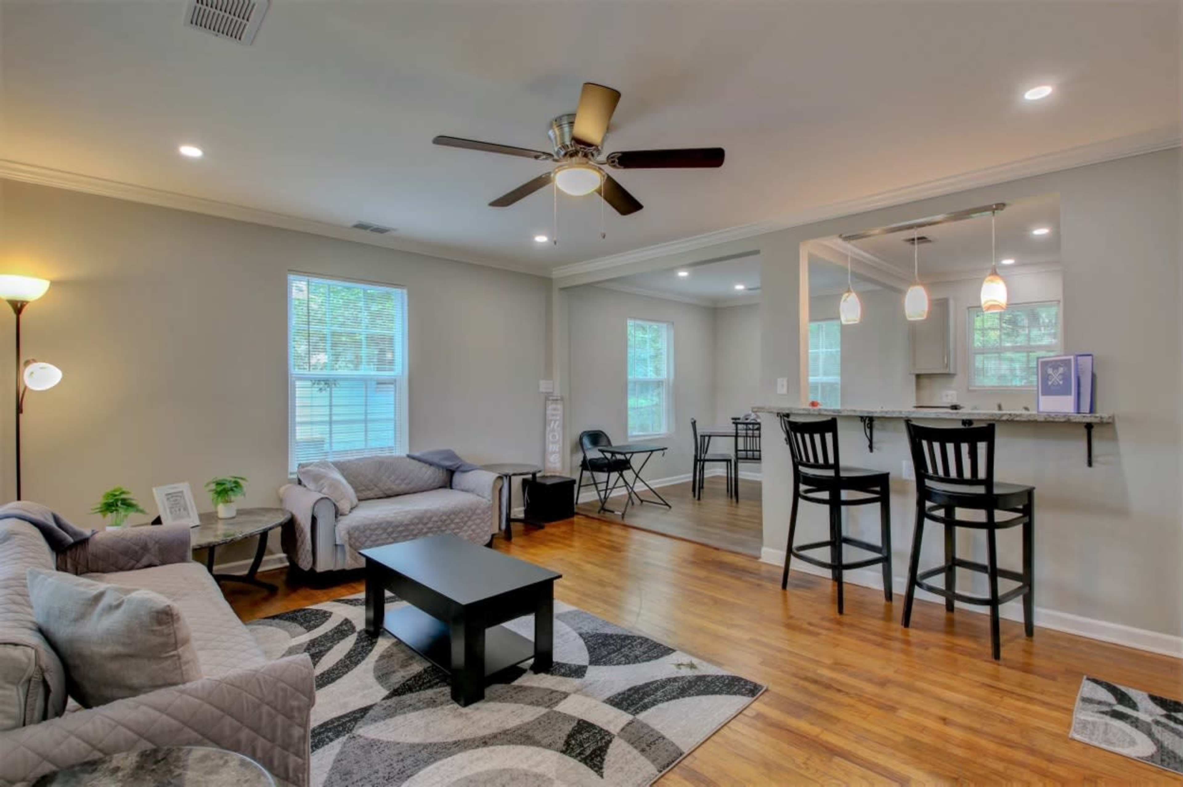 A living area with a sofa and chairs, a coffee table, and a ceiling fan, leading to an adjoining dining area with a table and chairs.