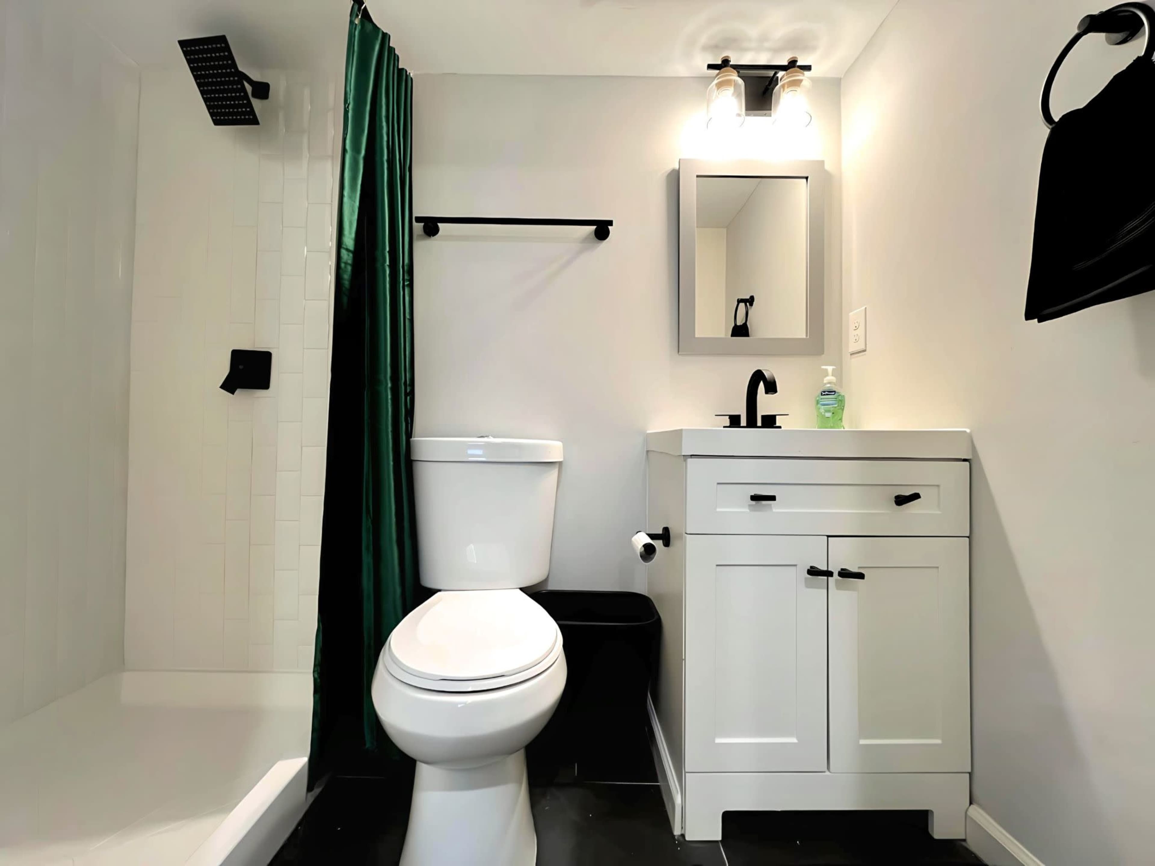 A compact bathroom with a shower, toilet, small vanity, and a mirror, featuring black and white decor along with a green shower curtain.
