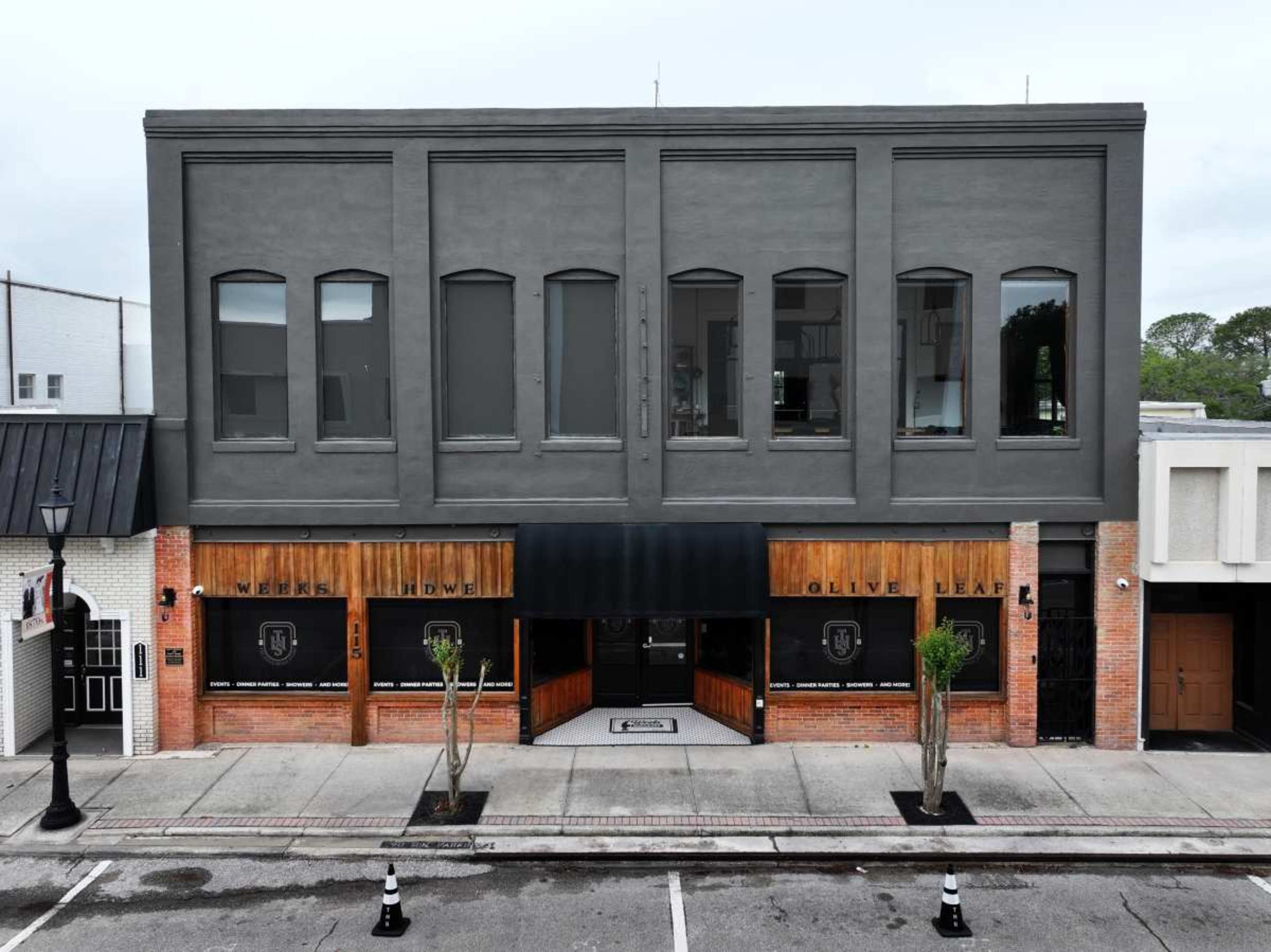 The image shows a three-story building with a gray façade and wooden accents, featuring two business entrances at the ground level under a black awning.