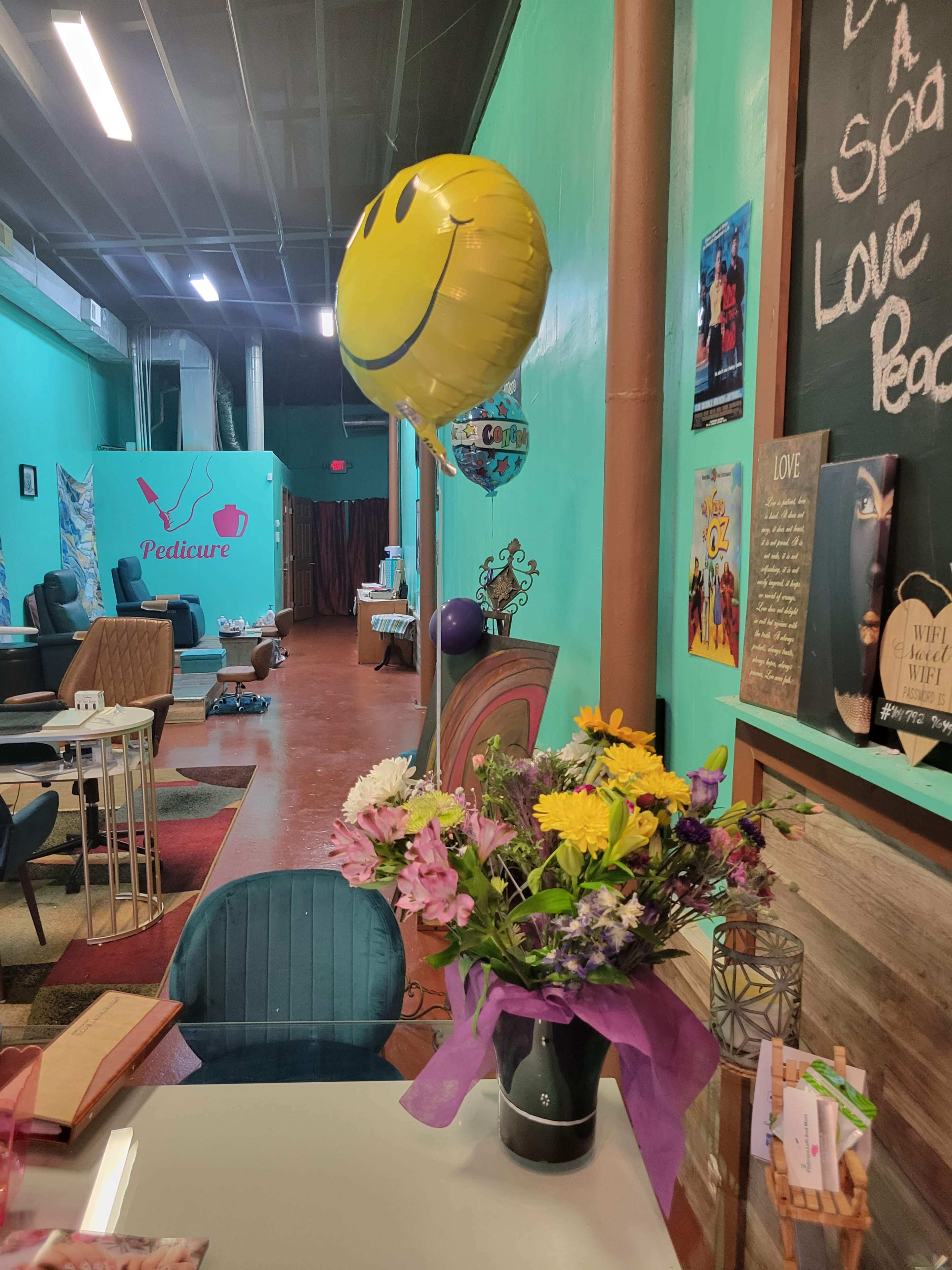 A colorful interior of a spa or salon, featuring a table with a bouquet of flowers, a smiling balloon, and decorative walls.