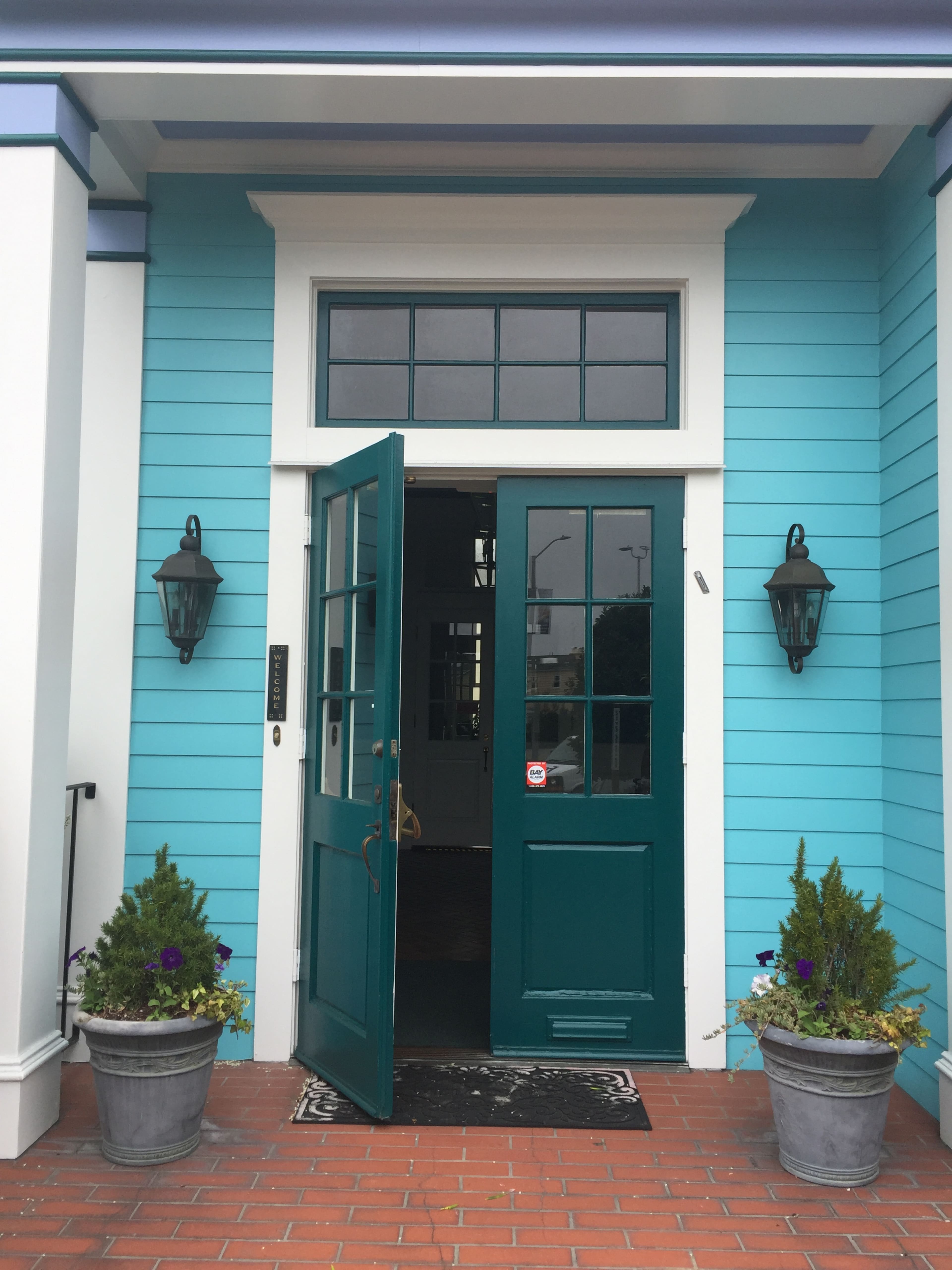 An entrance to a building with a turquoise facade, featuring an open double door and two lanterns mounted on either side.