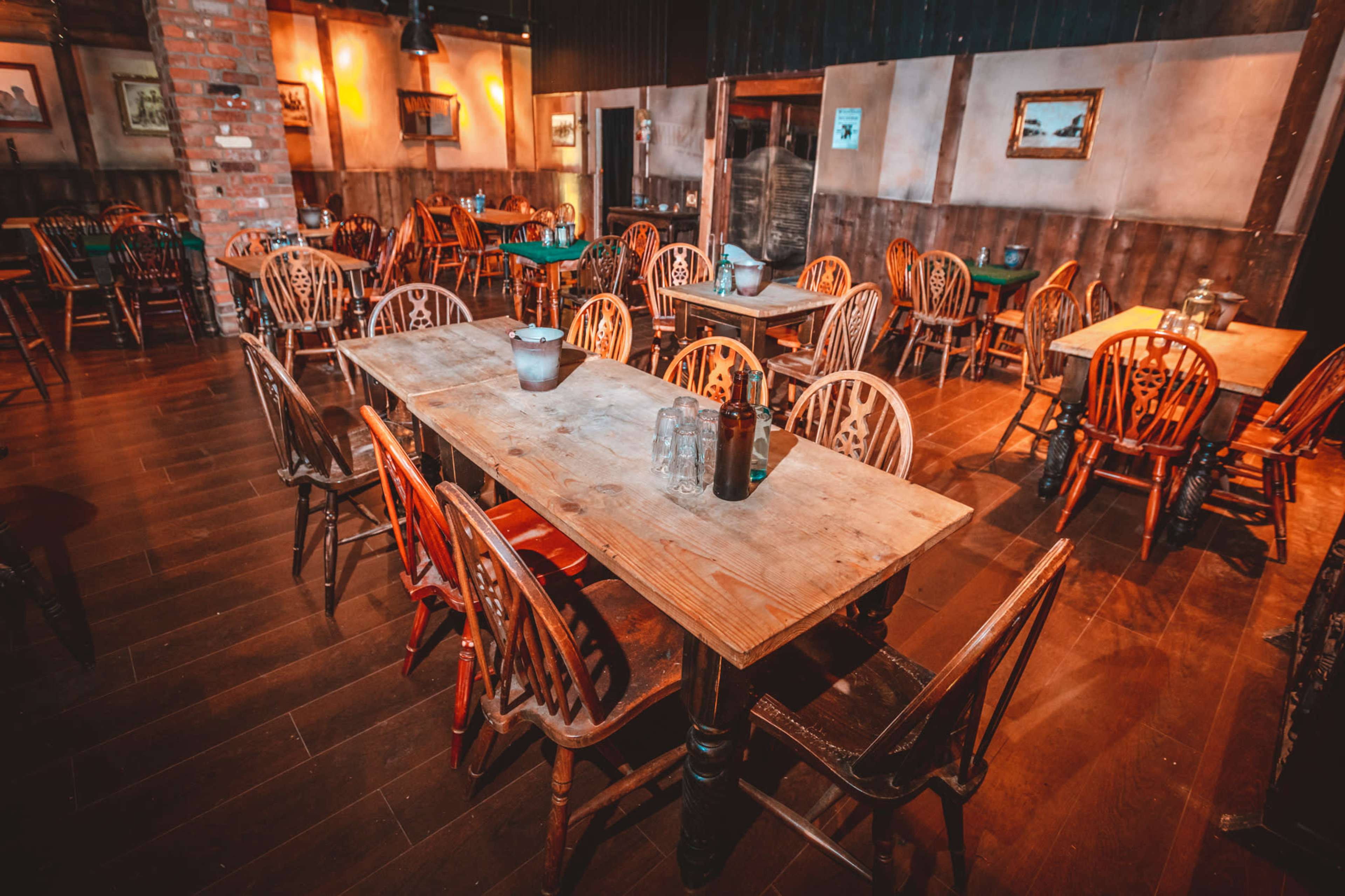 An empty rustic dining area with wooden tables and chairs arranged around a dimly lit room.