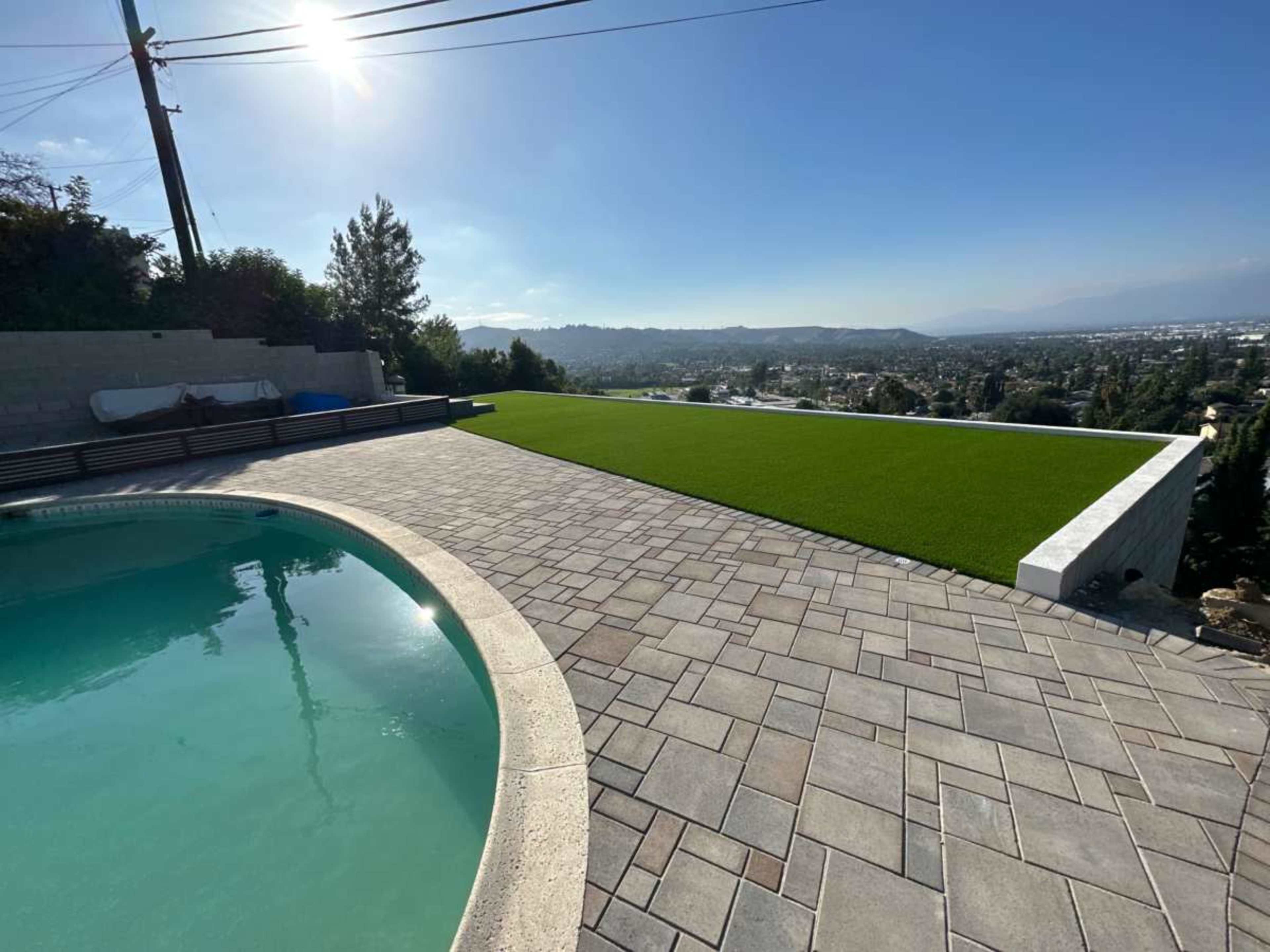 The image shows a backyard with a swimming pool and a large area of artificial grass overlooking a hilly landscape.