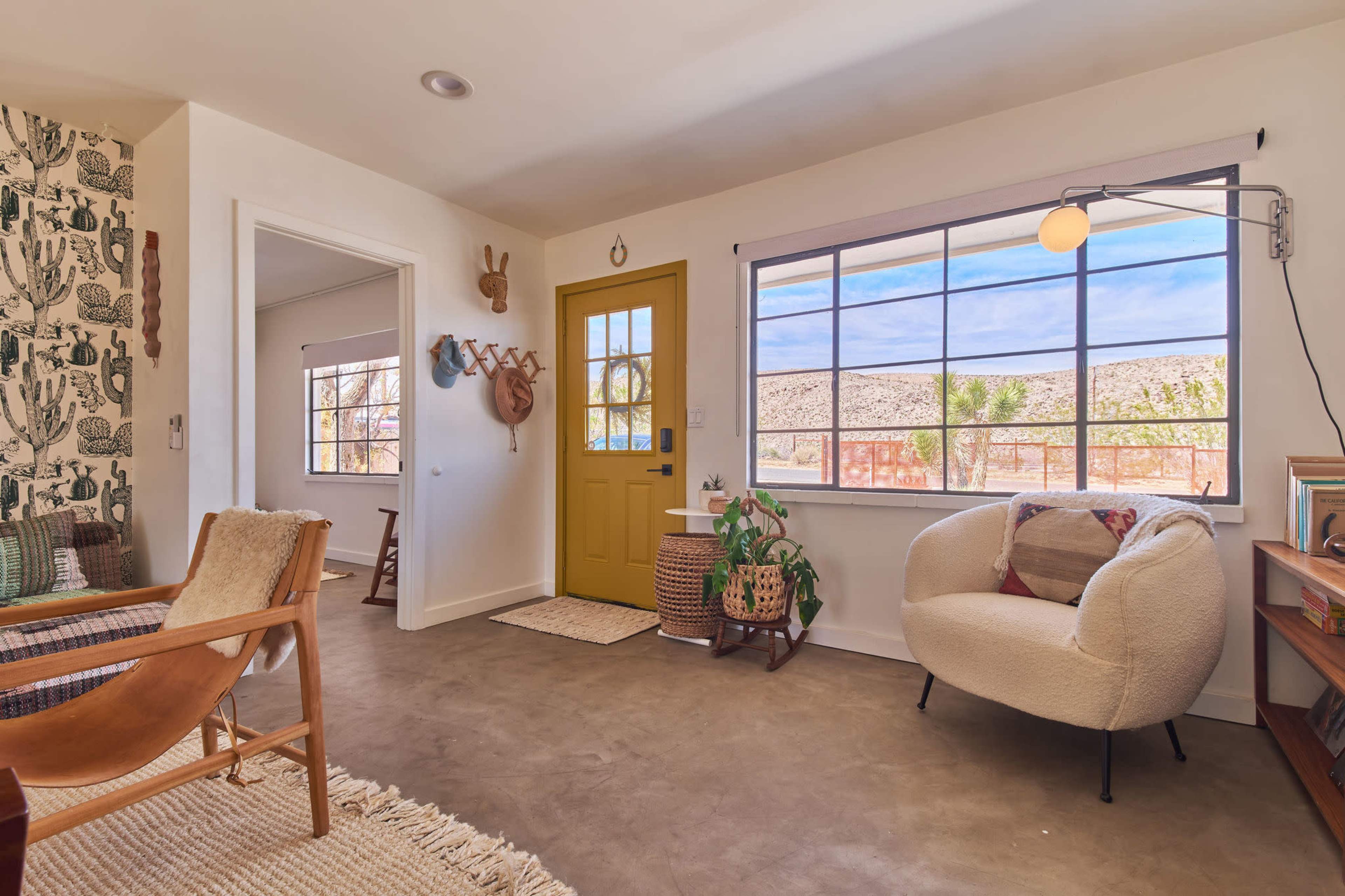 A bright, inviting interior space featuring a yellow front door, a cozy seating area, and large windows allowing natural light to flow in.