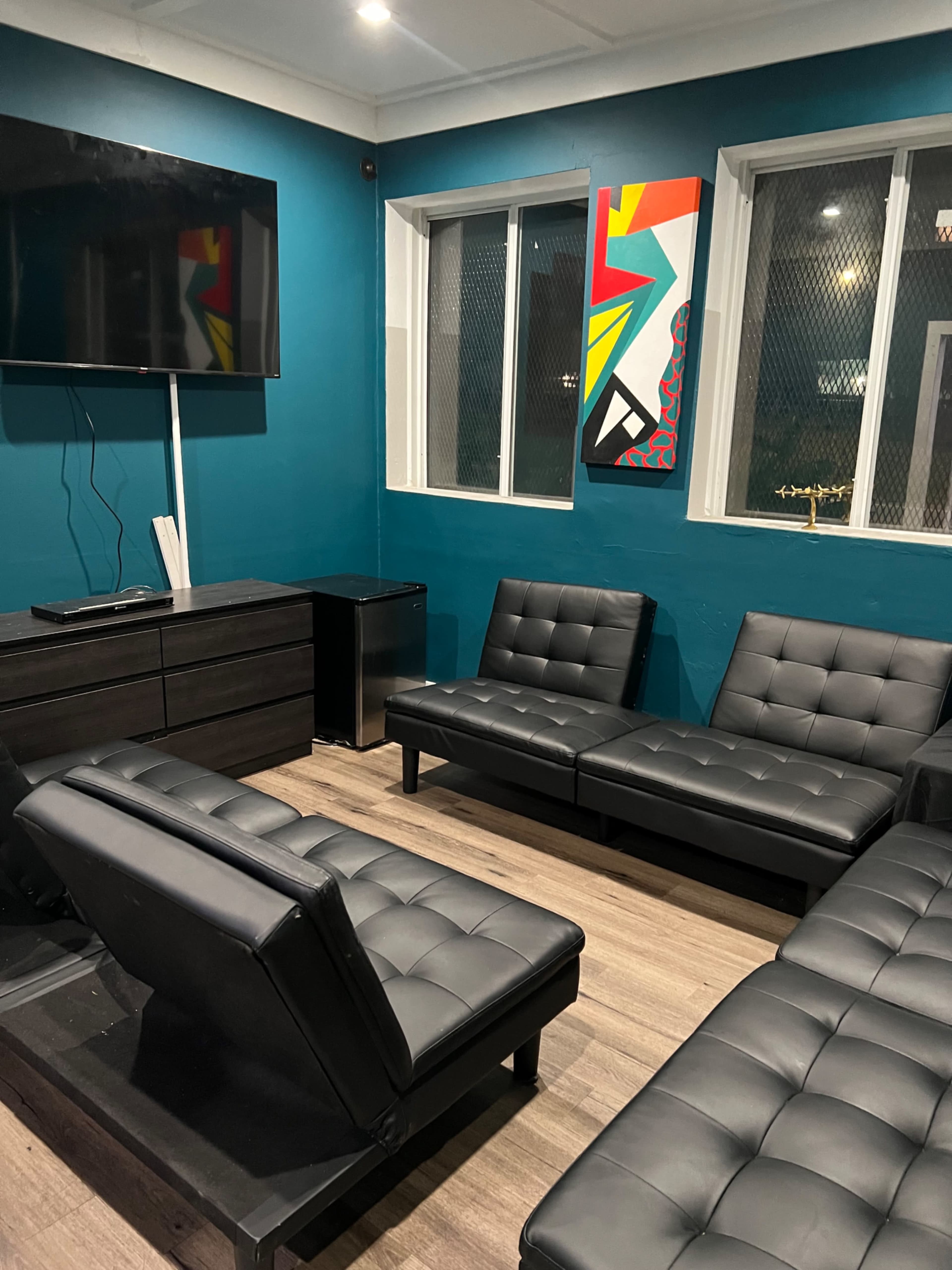 The image shows a waiting room with black leather couches, a TV mounted on a teal wall, and a colorful artwork hanging above a window.