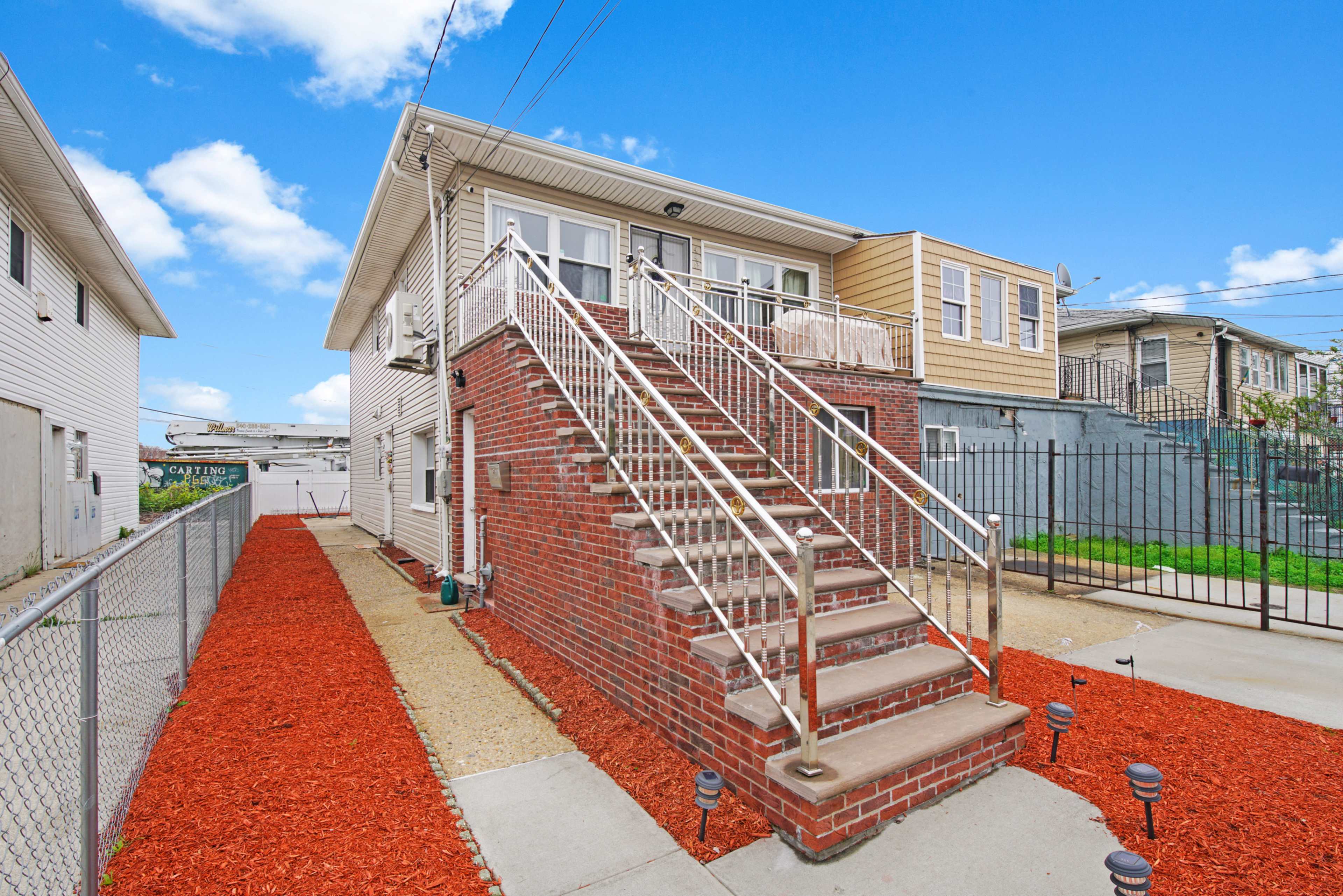 A two-story brick building with a set of stairs leading to the entrance, surrounded by a gravel path and red mulch landscaping.