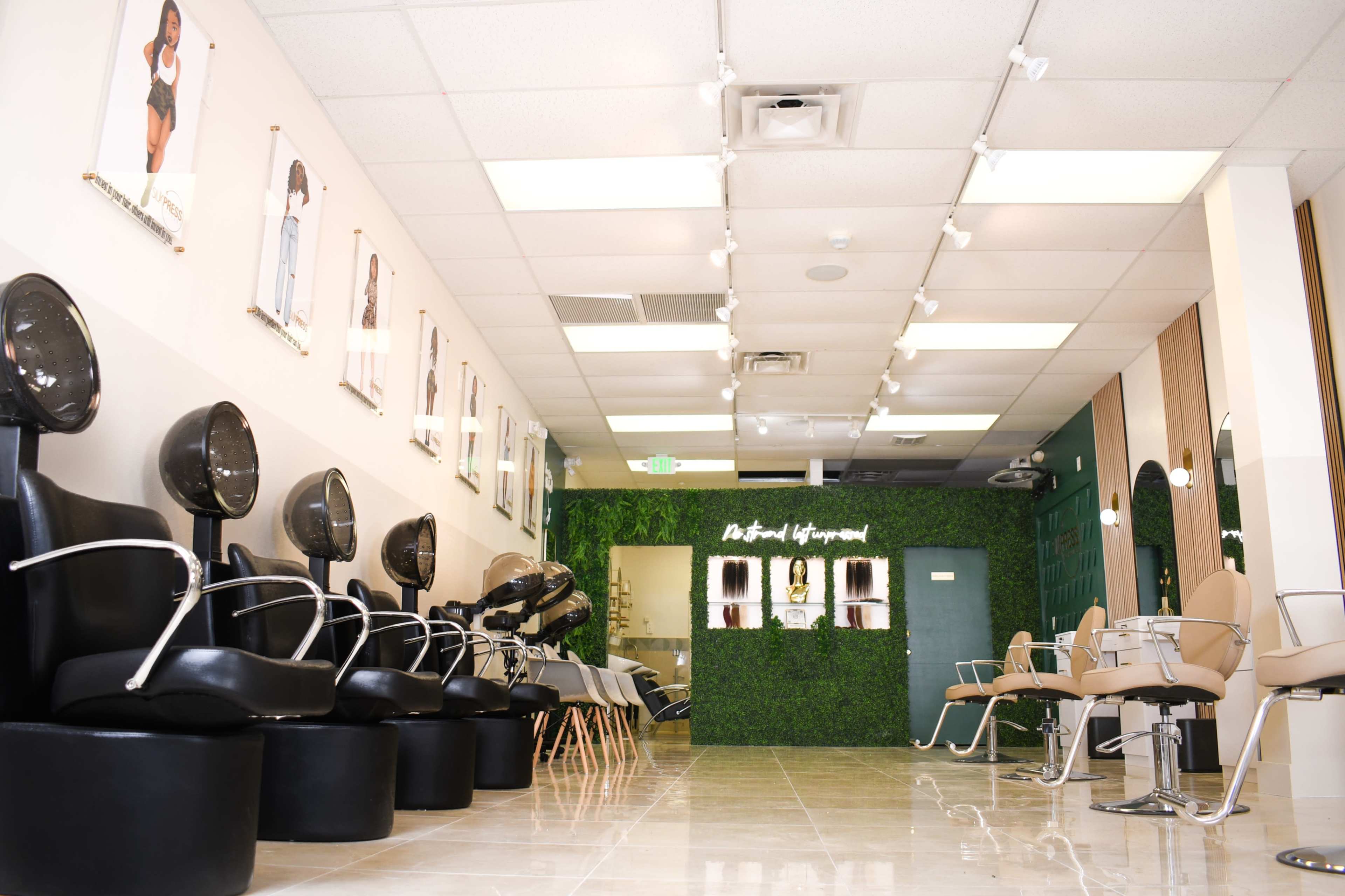 A modern salon interior with black styling chairs, hairdryers, and a green wall with the words "A Hair Legend" prominently displayed.