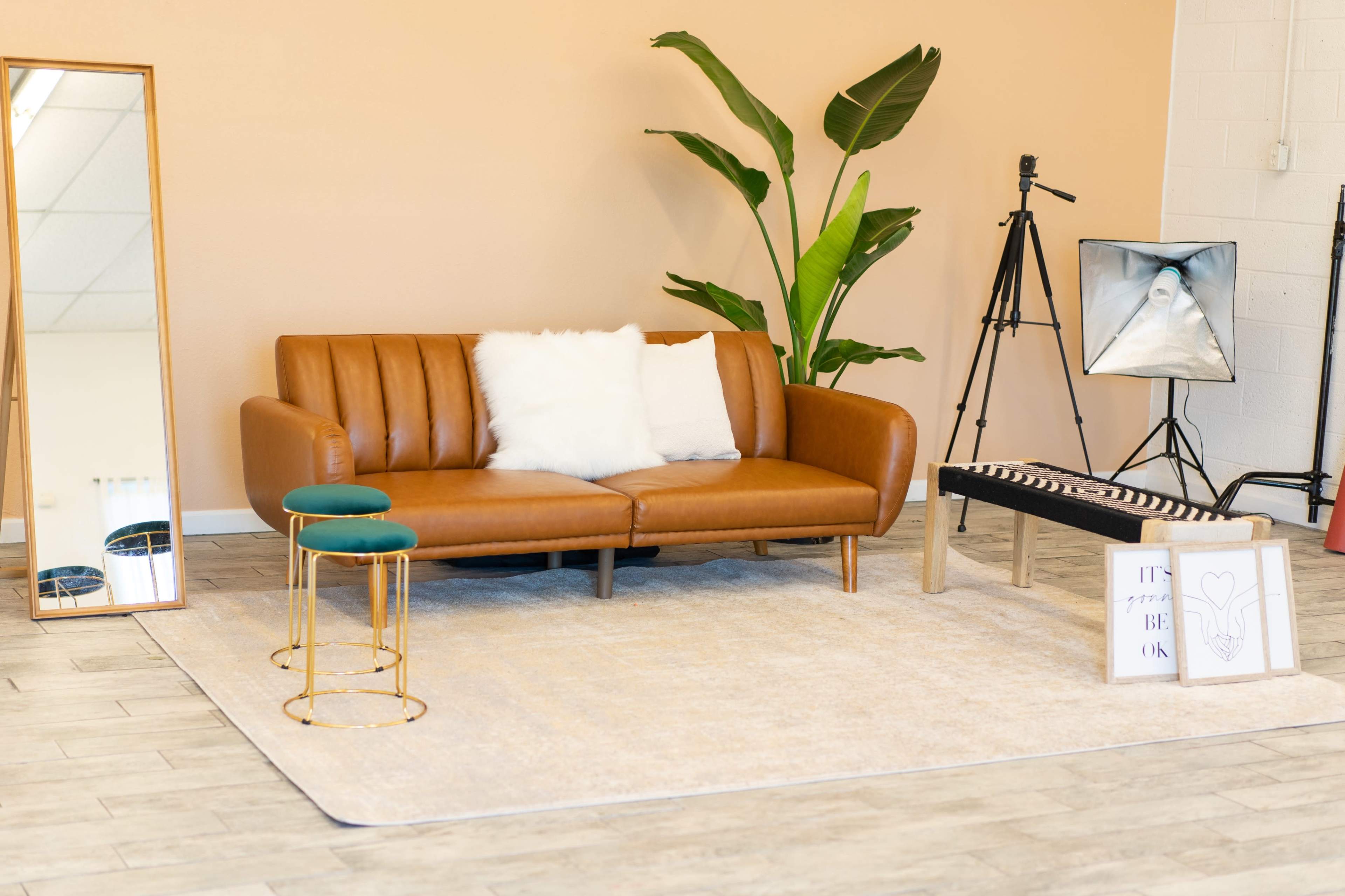 A modern living room setup with a brown leather sofa, two green-accented side tables, a large mirror, a plant, and a small coffee table with decorative items.