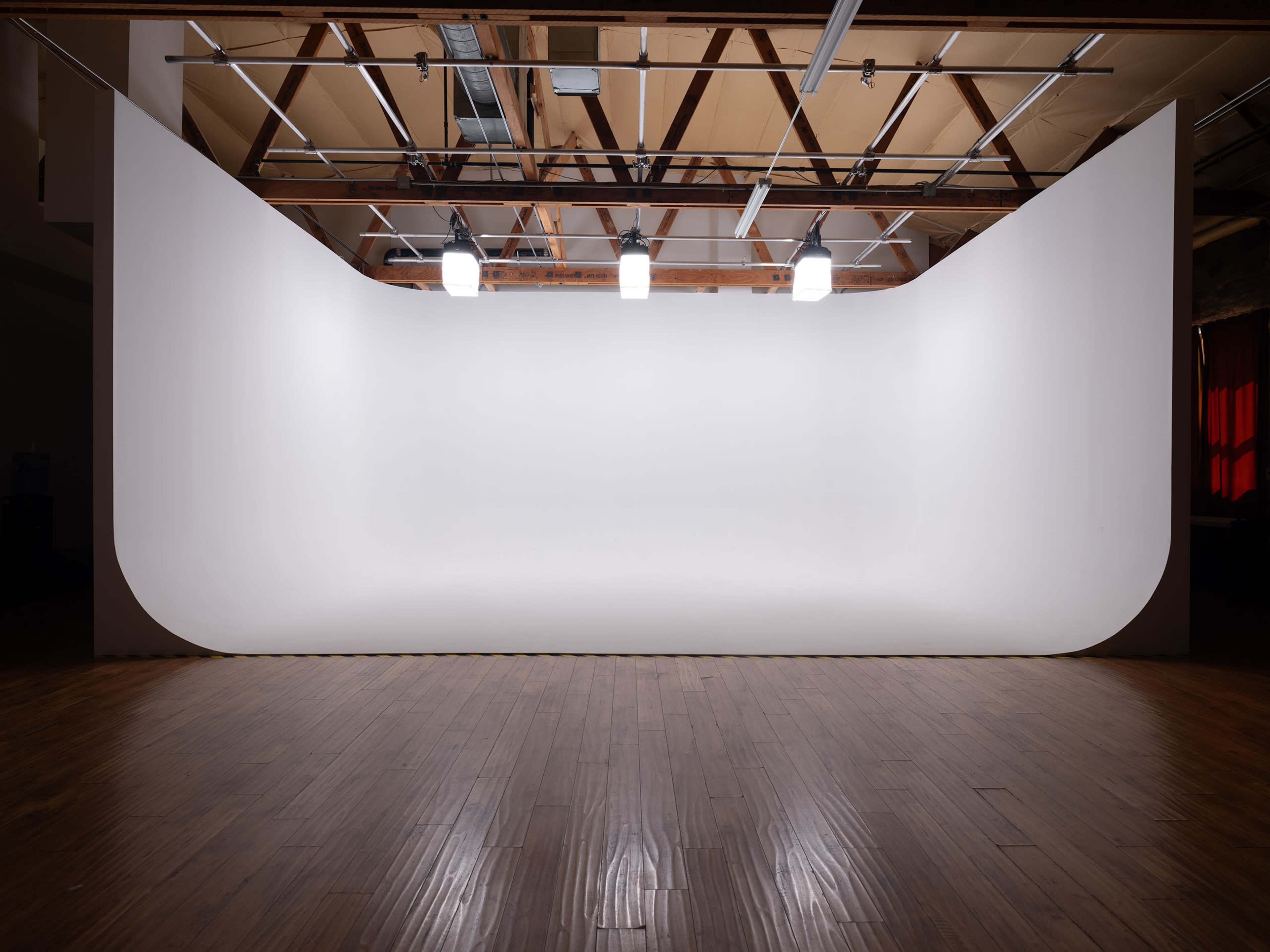 The image shows a photography studio with a seamless white backdrop and bright overhead lights illuminating the space.