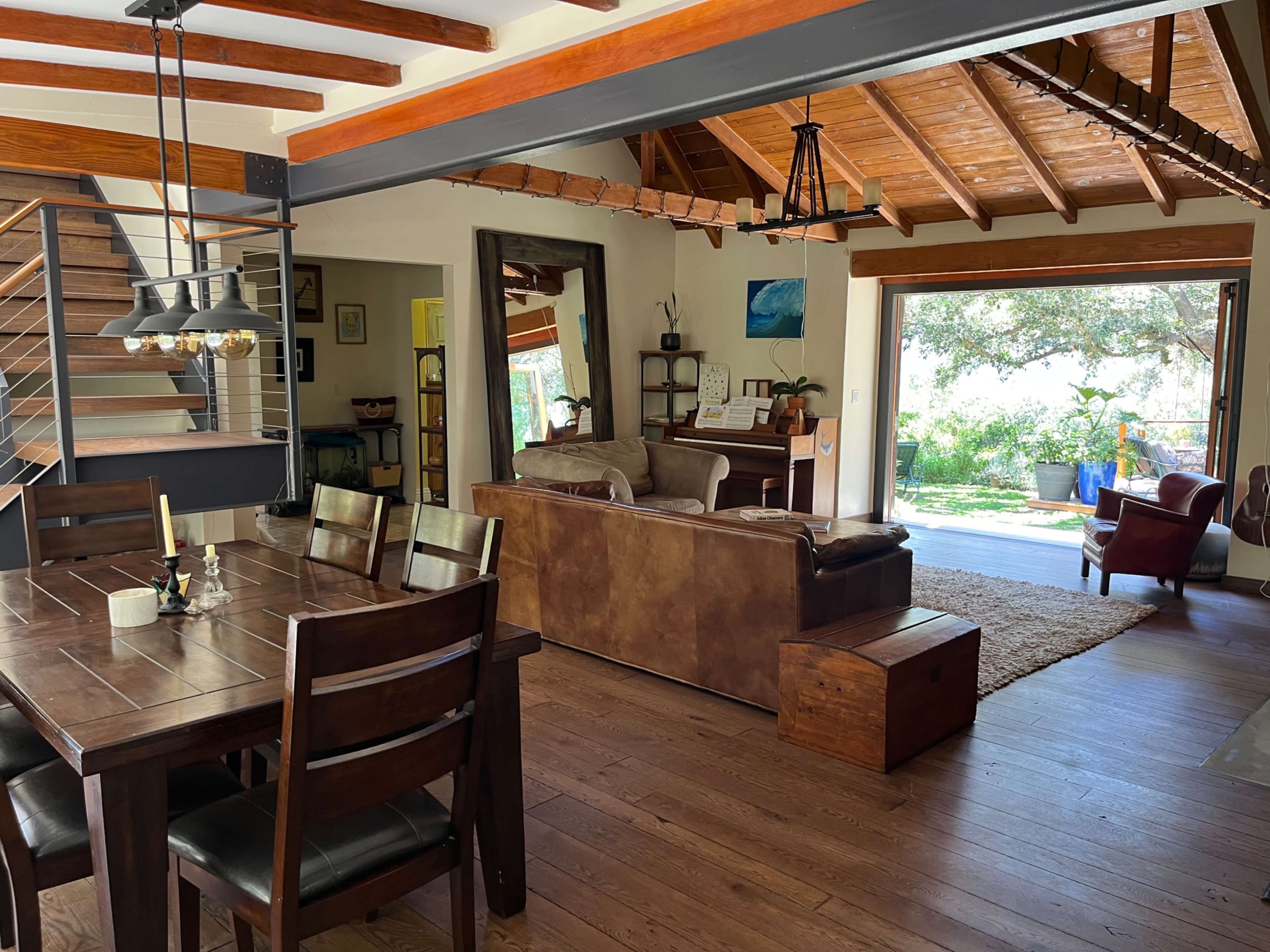 A spacious living area features a dining table, a leather sofa, and an open doorway leading to a garden.