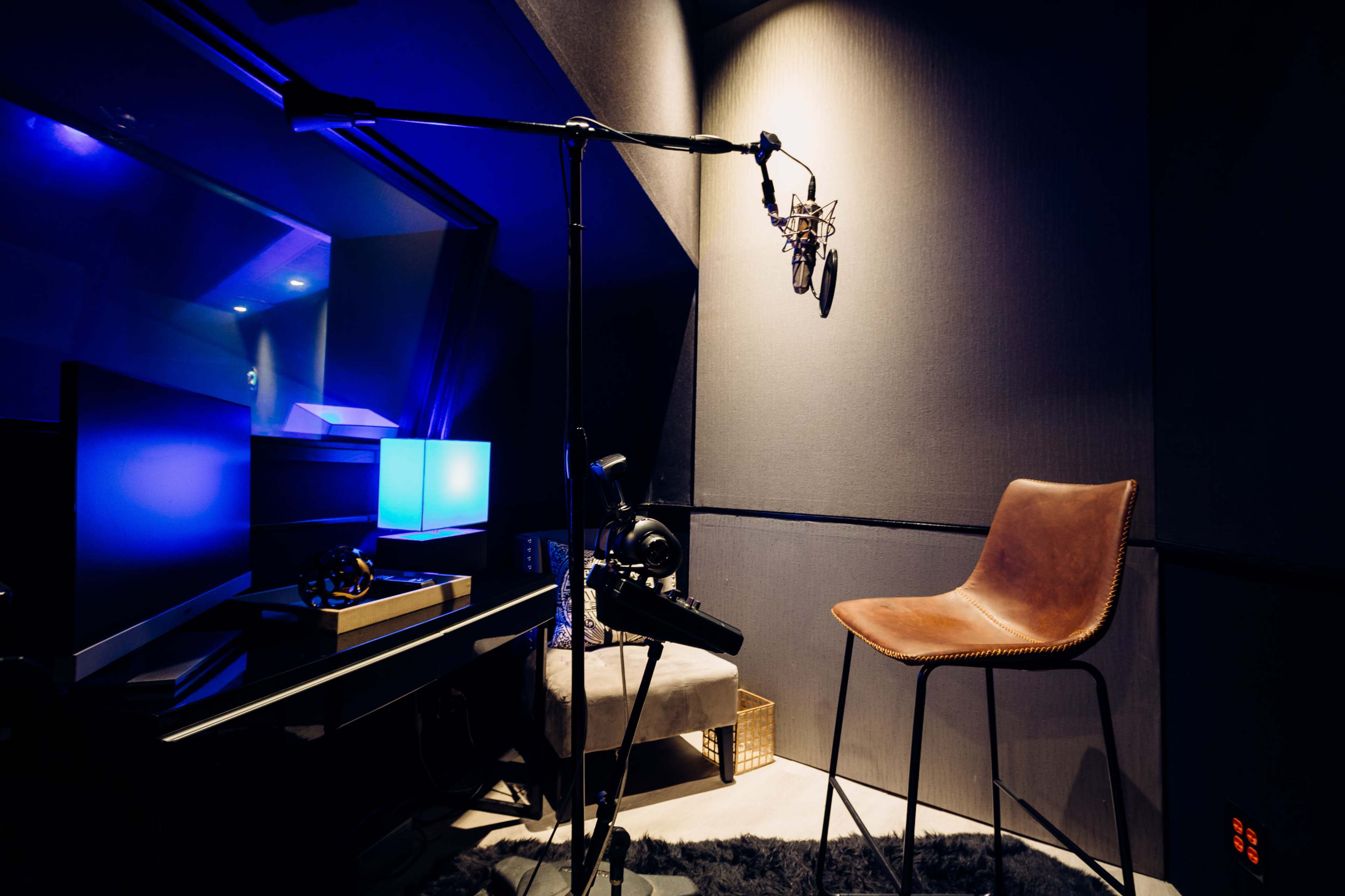 A recording studio booth featuring a microphone on a stand, a chair, and ambient lighting.