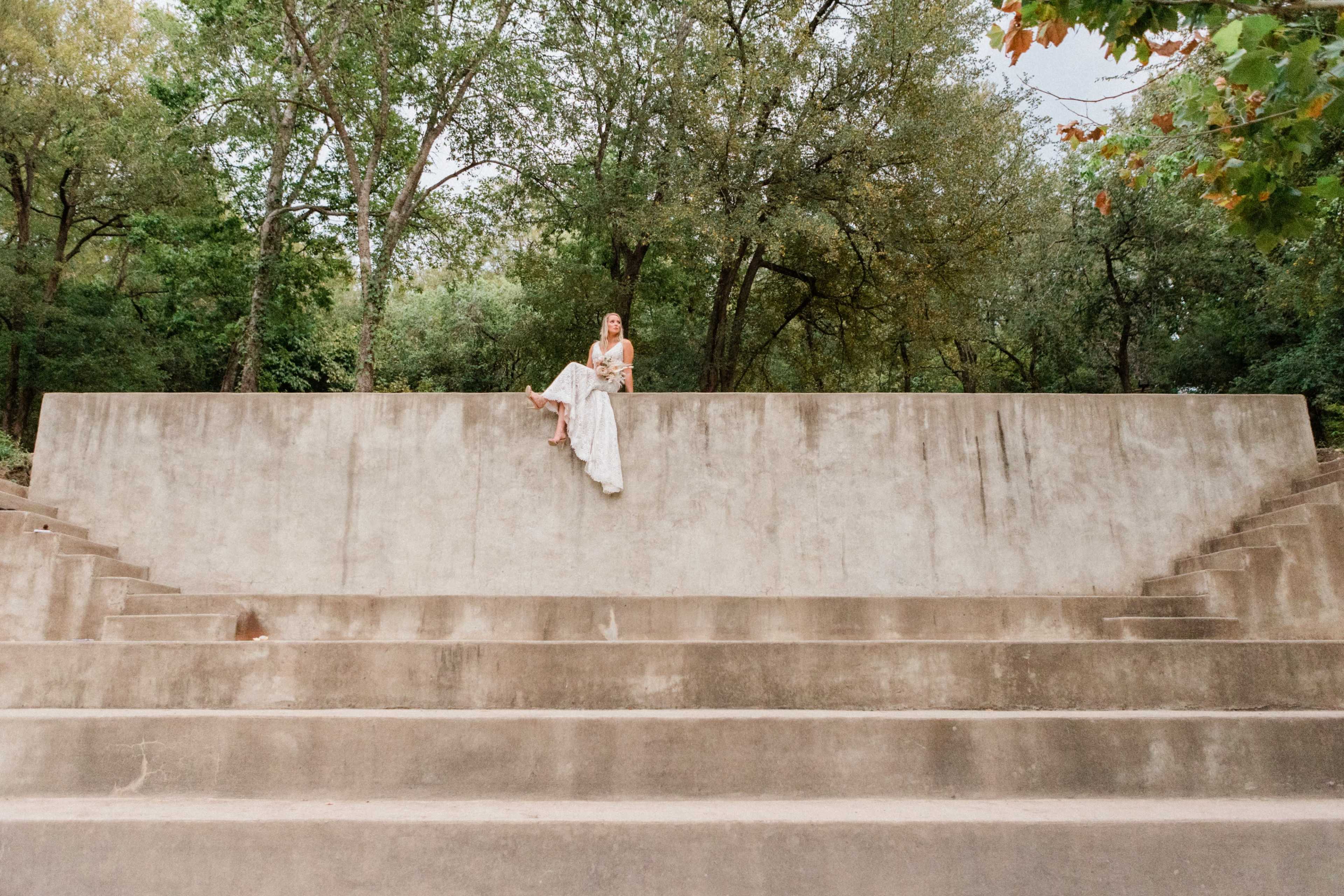 A person sits on a concrete bench structure surrounded by trees.