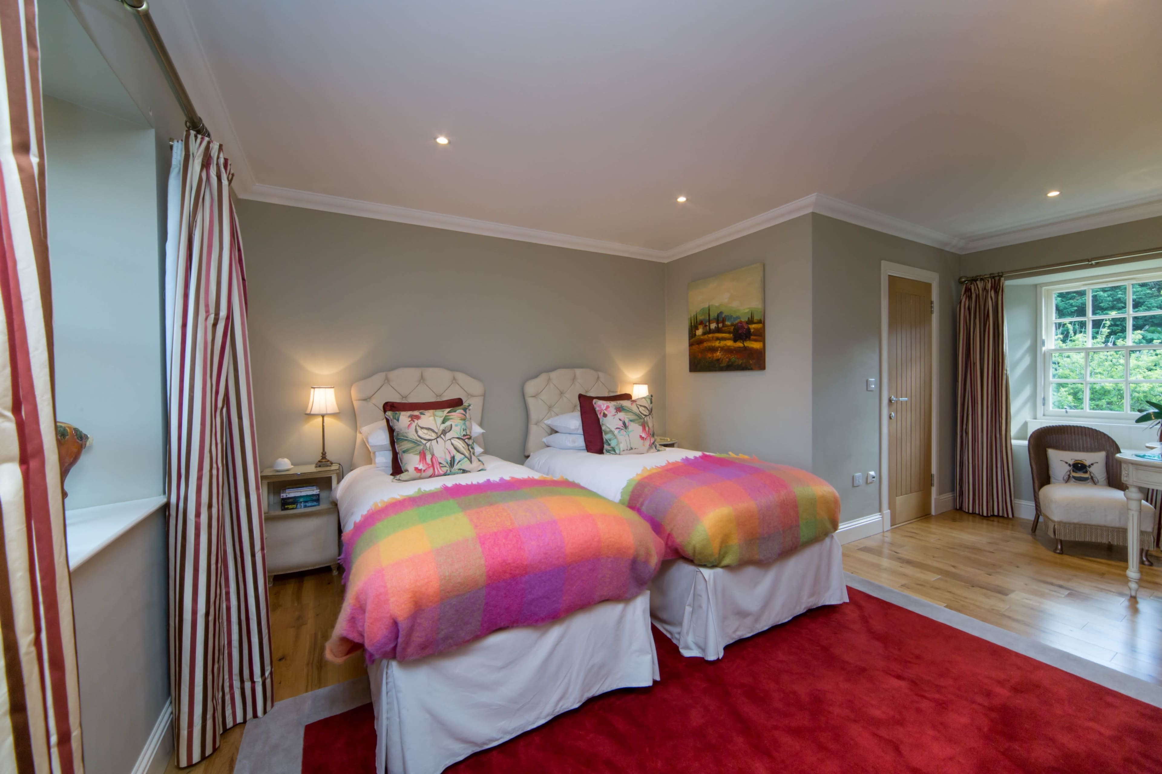 A well-furnished guest room with two twin beds, each covered with a colorful blanket, and a red area rug on the wooden floor.