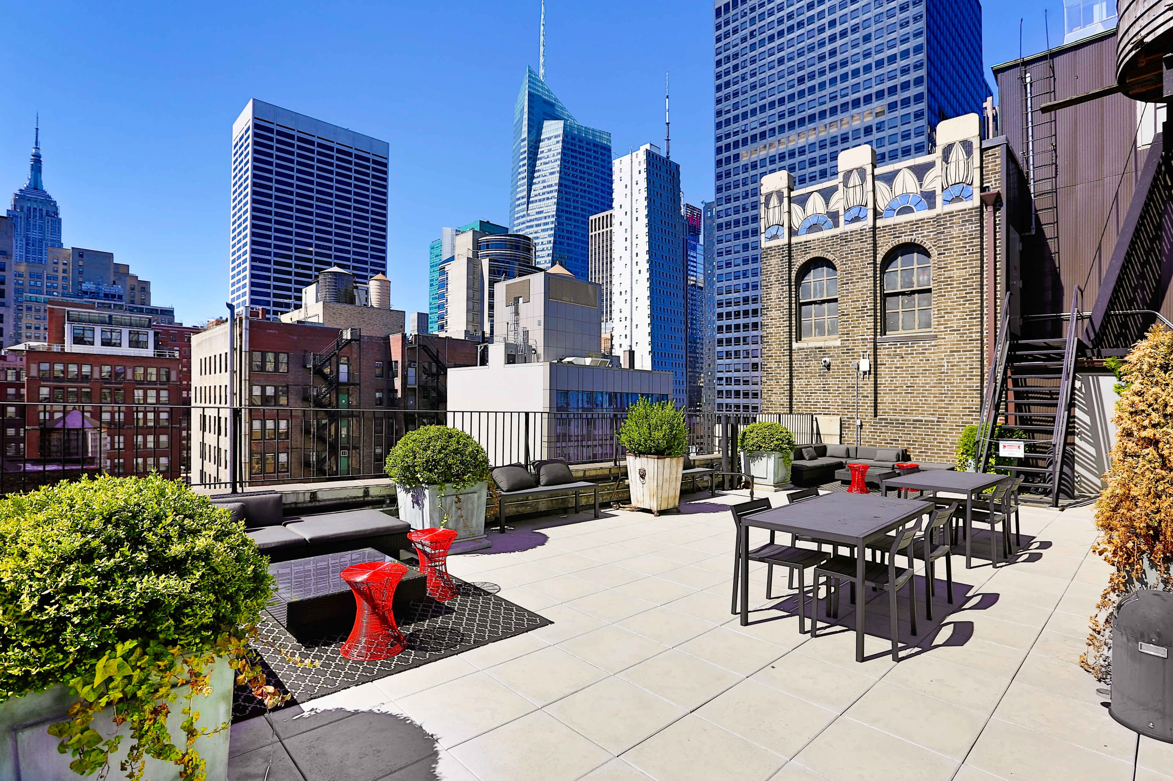 The rooftop terrace features modern seating and dining areas with views of skyscrapers in a bustling city skyline.