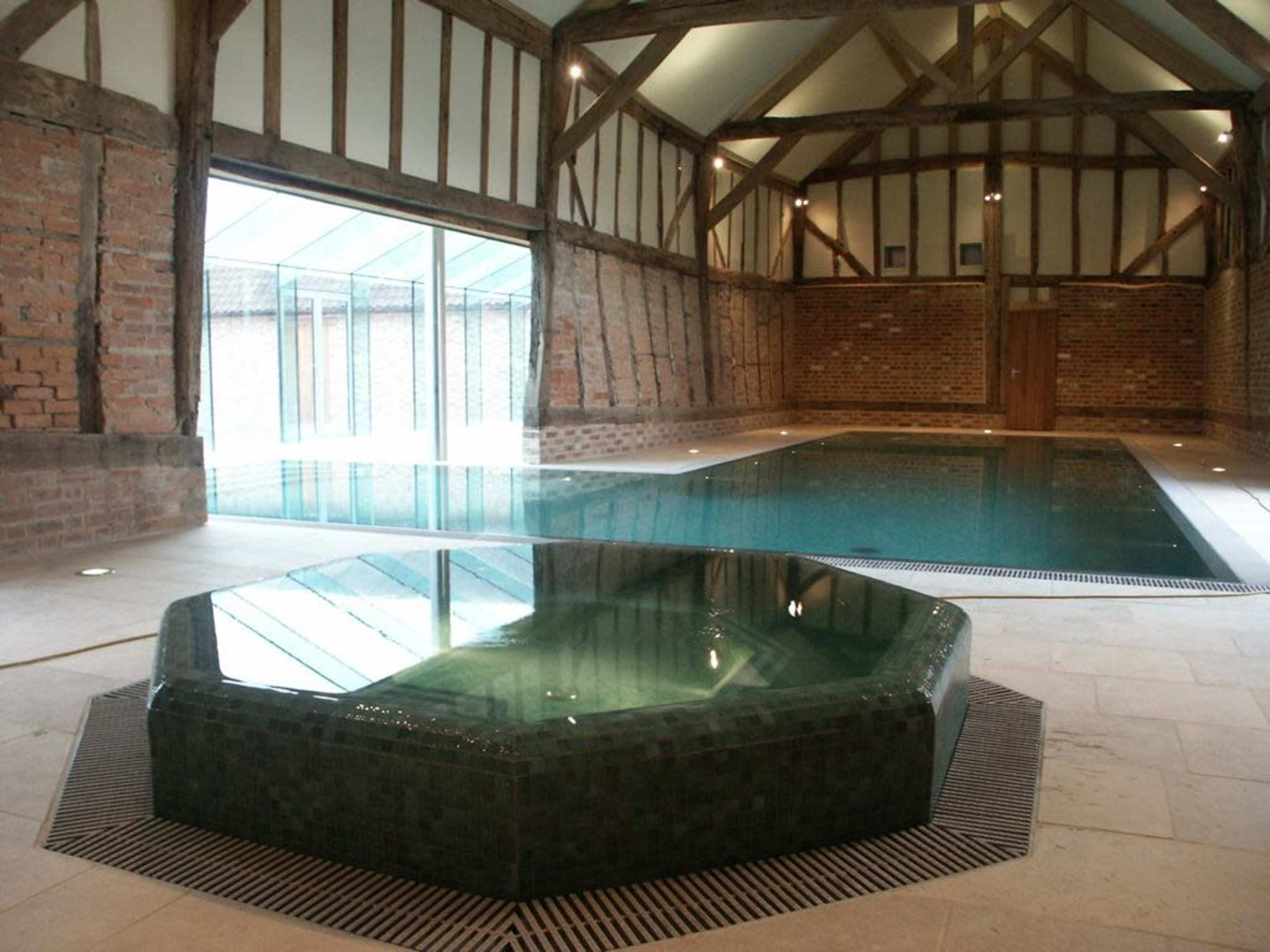 A spacious indoor swimming pool area with a large octagonal spa in one corner, surrounded by brick and wooden walls.
