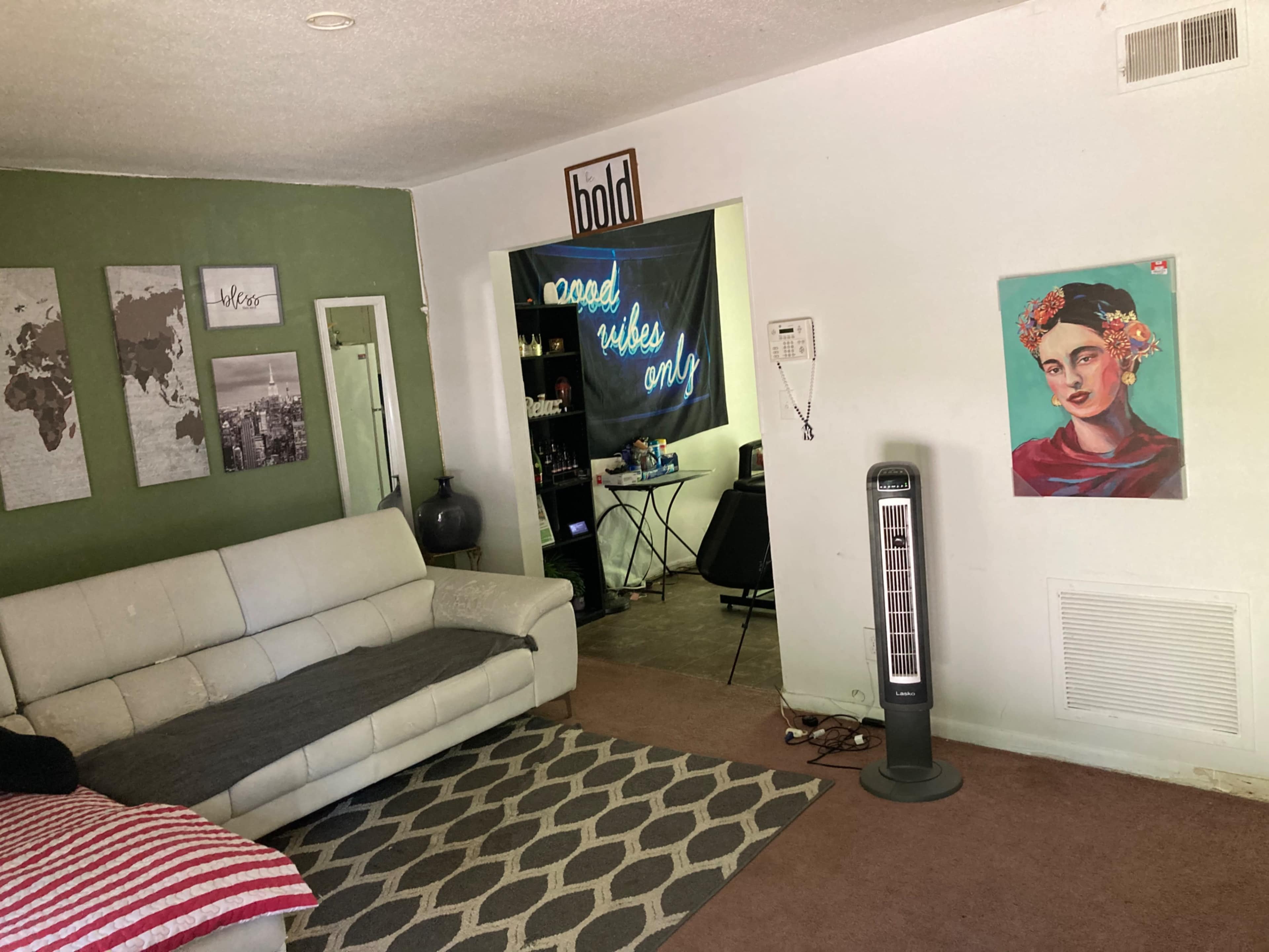 A living room with a white sectional couch, a rug with a geometric pattern, and a wall adorned with a portrait of a woman and various framed prints.