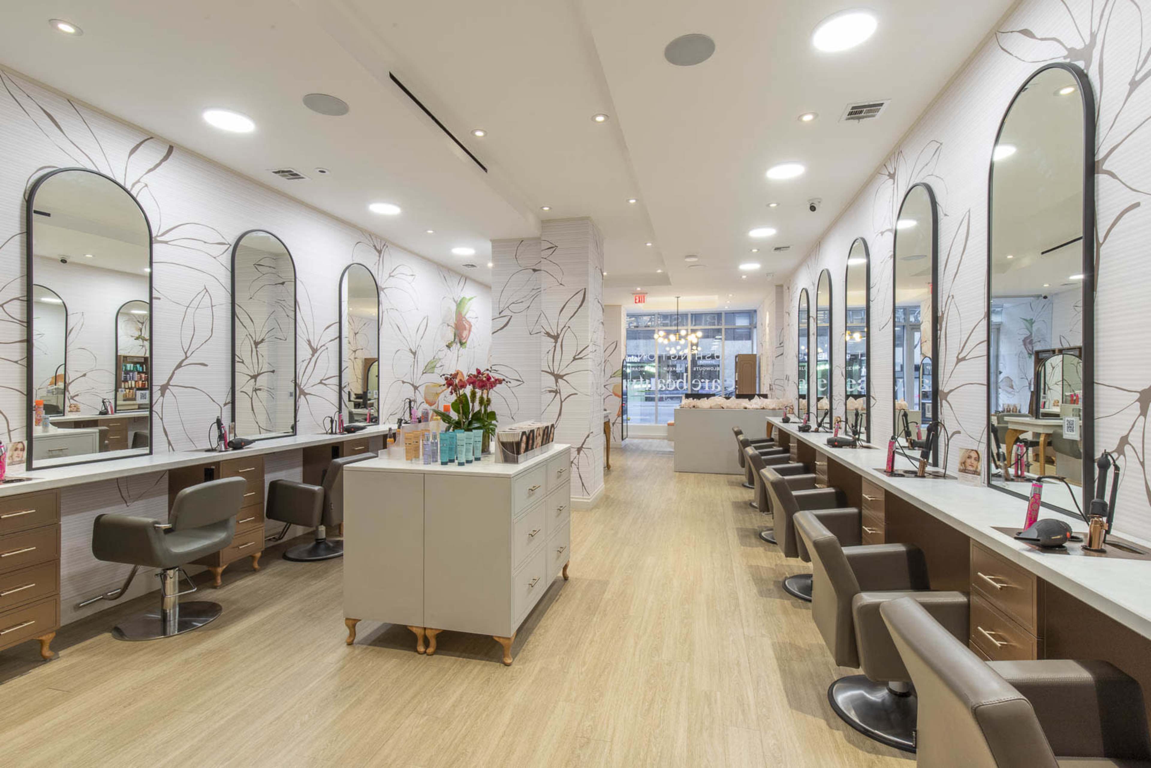 The image shows a modern hair and beauty salon featuring multiple styling stations with large mirrors, a central reception area, and decorative wall patterns.