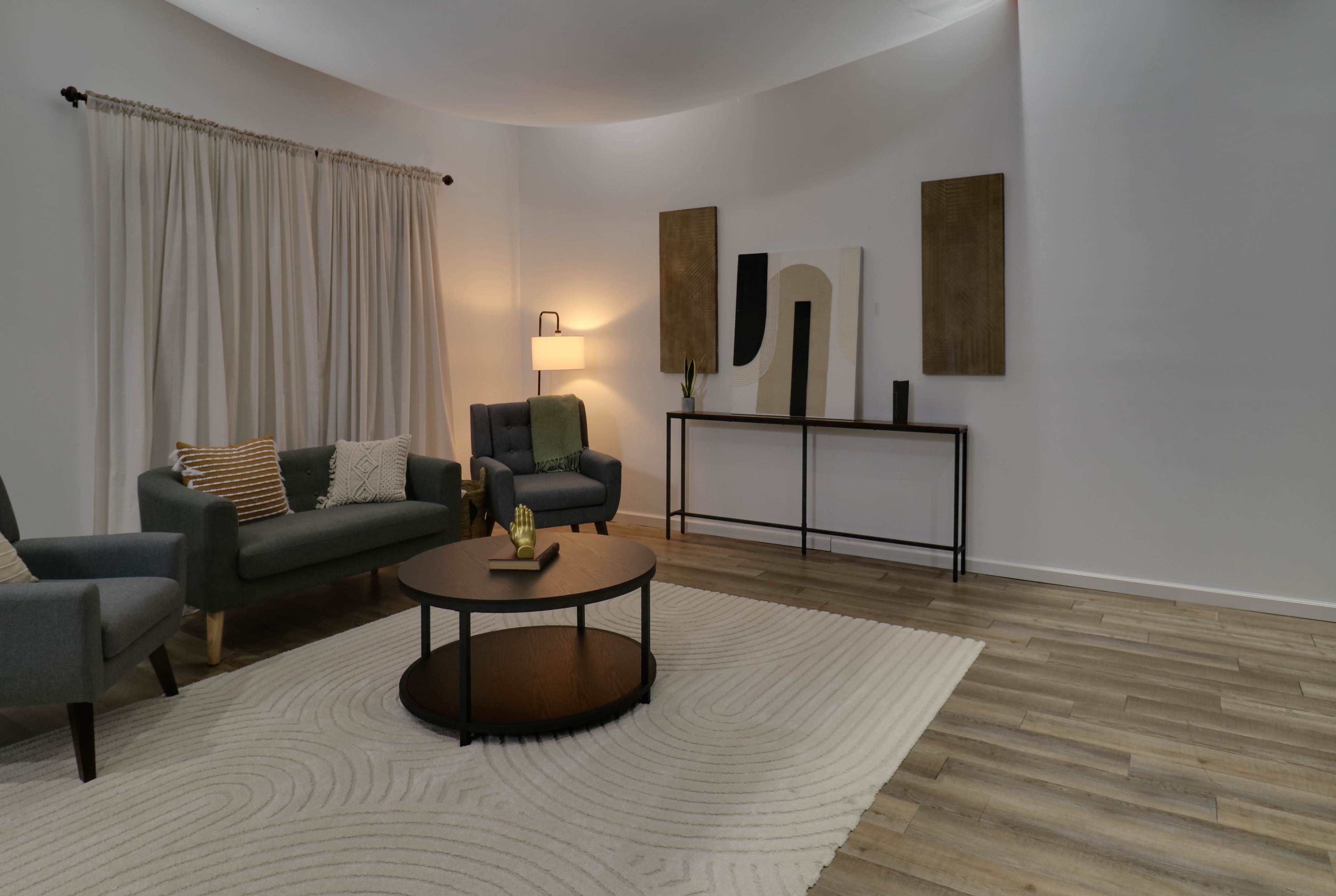 The image shows a modern living room with a circular coffee table, two armchairs, a sofa, and decorative art pieces on the wall.