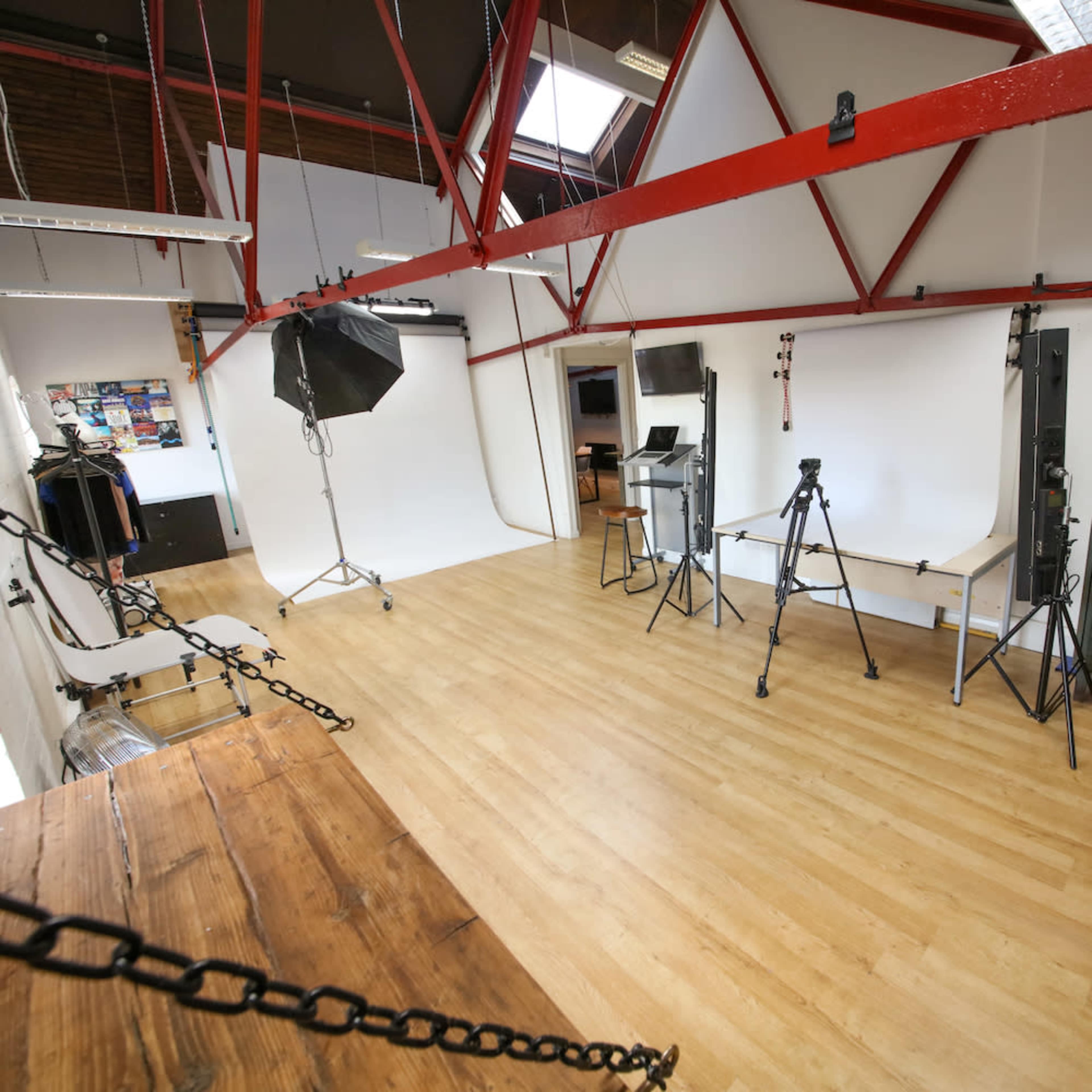 A spacious photography studio featuring a wooden floor, white backdrops, studio lights, and equipment arranged throughout the space.