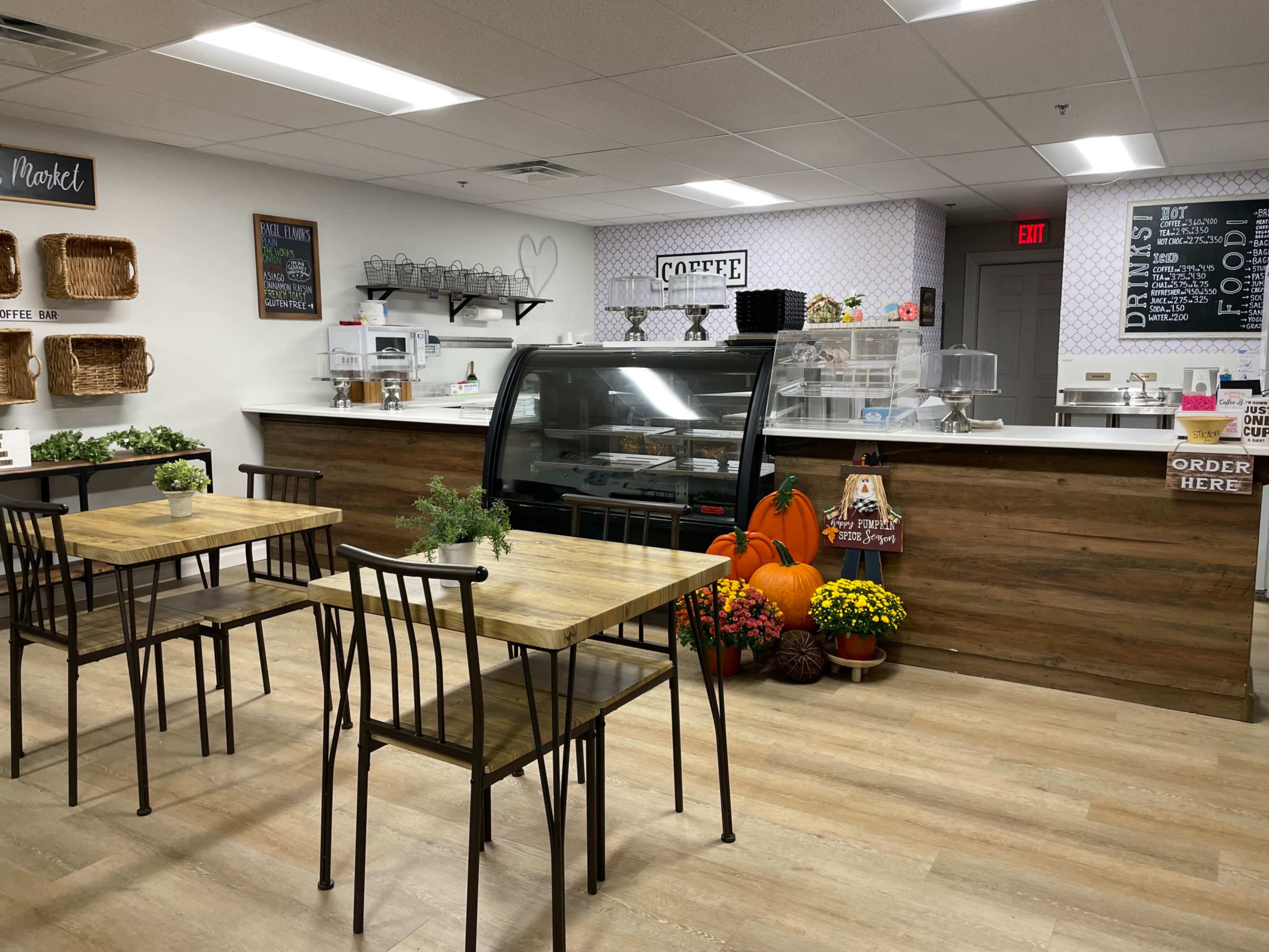 A cafe interior featuring wooden tables and chairs, a display case, and seasonal decorations including pumpkins and flowers.