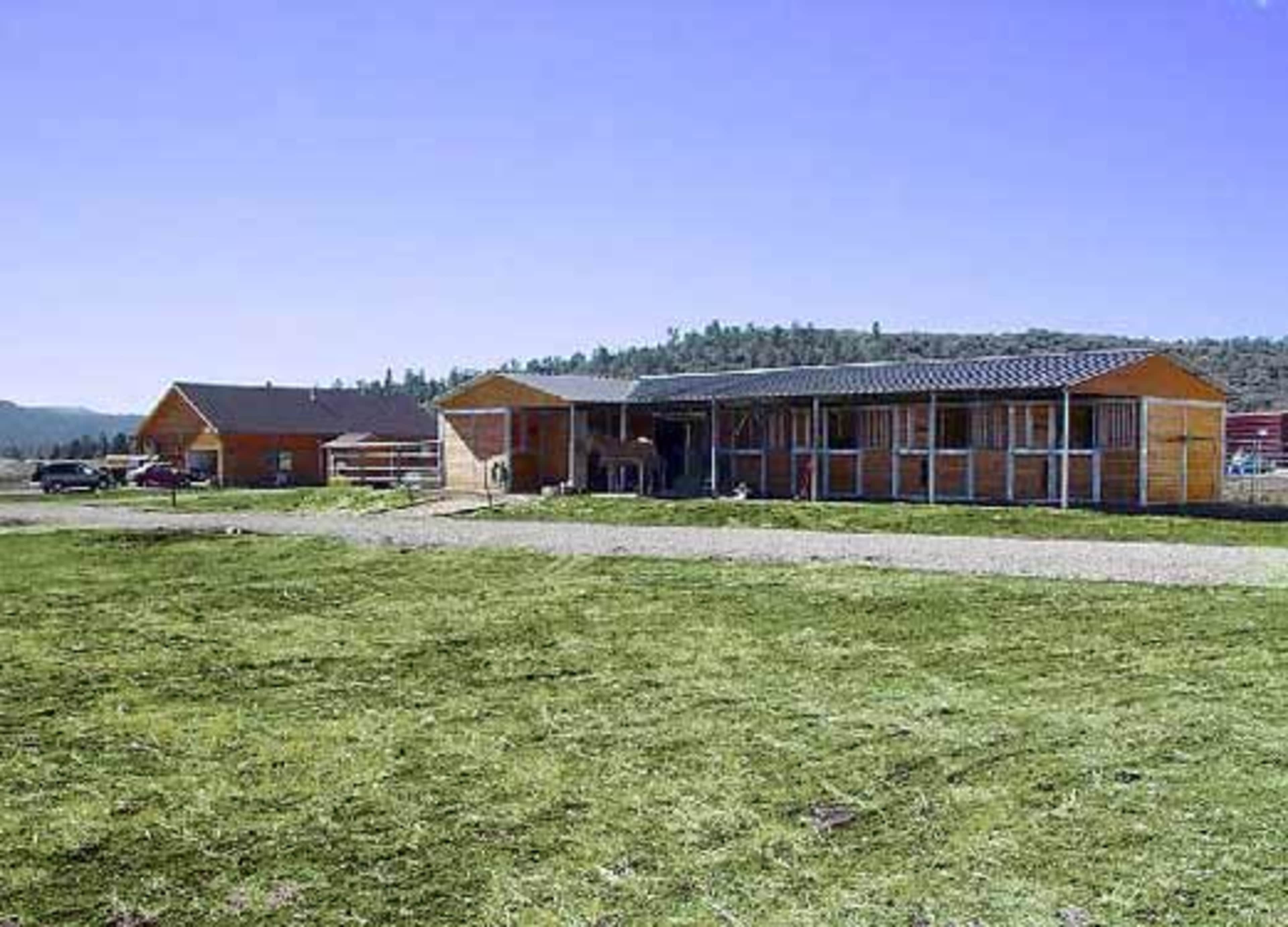 A ranch with wooden buildings set against a backdrop of hills under a clear blue sky.