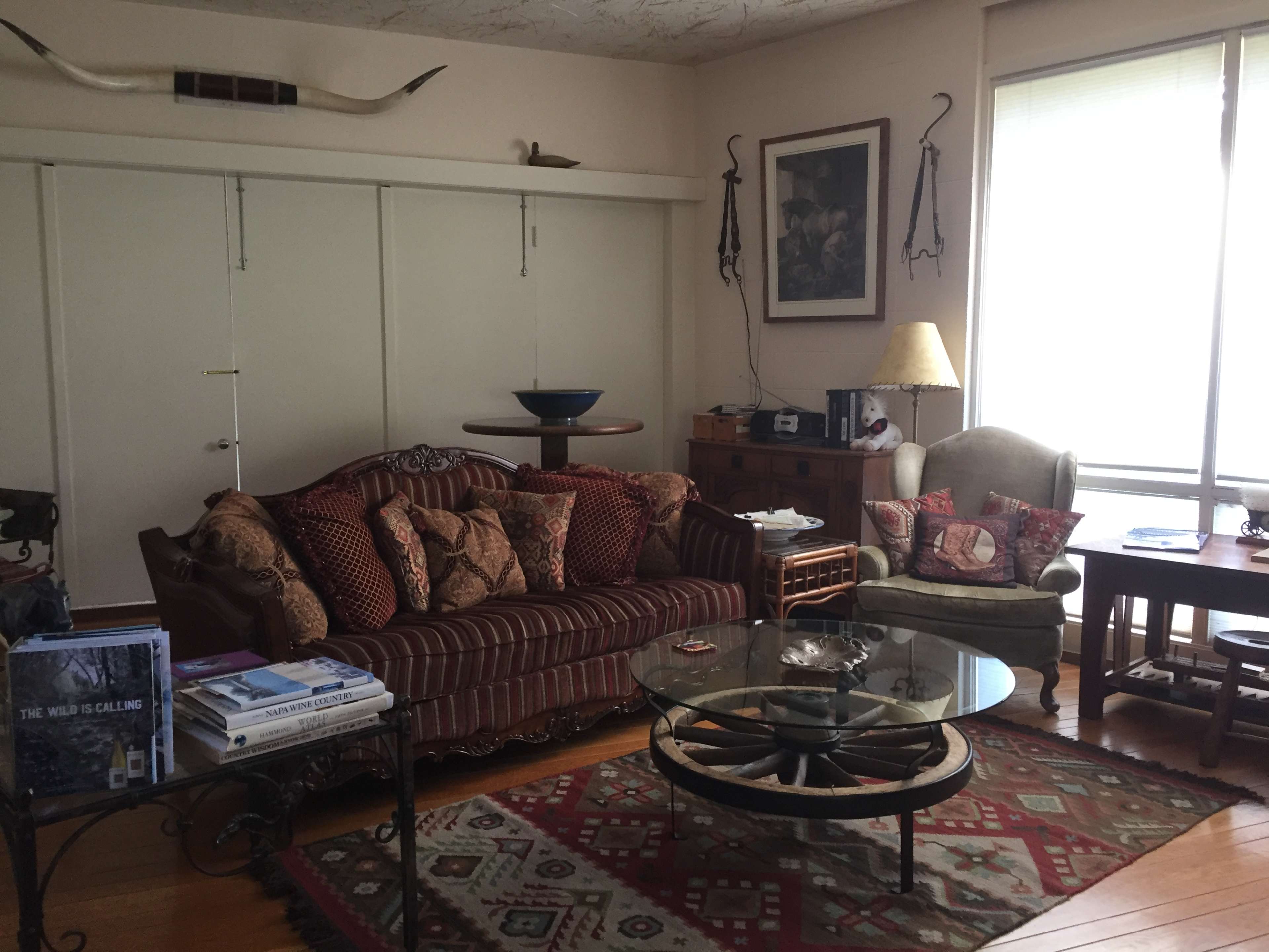 A living room with a striped sofa and armchair, a glass coffee table on a patterned rug, and a mix of decorative items on shelves and walls.