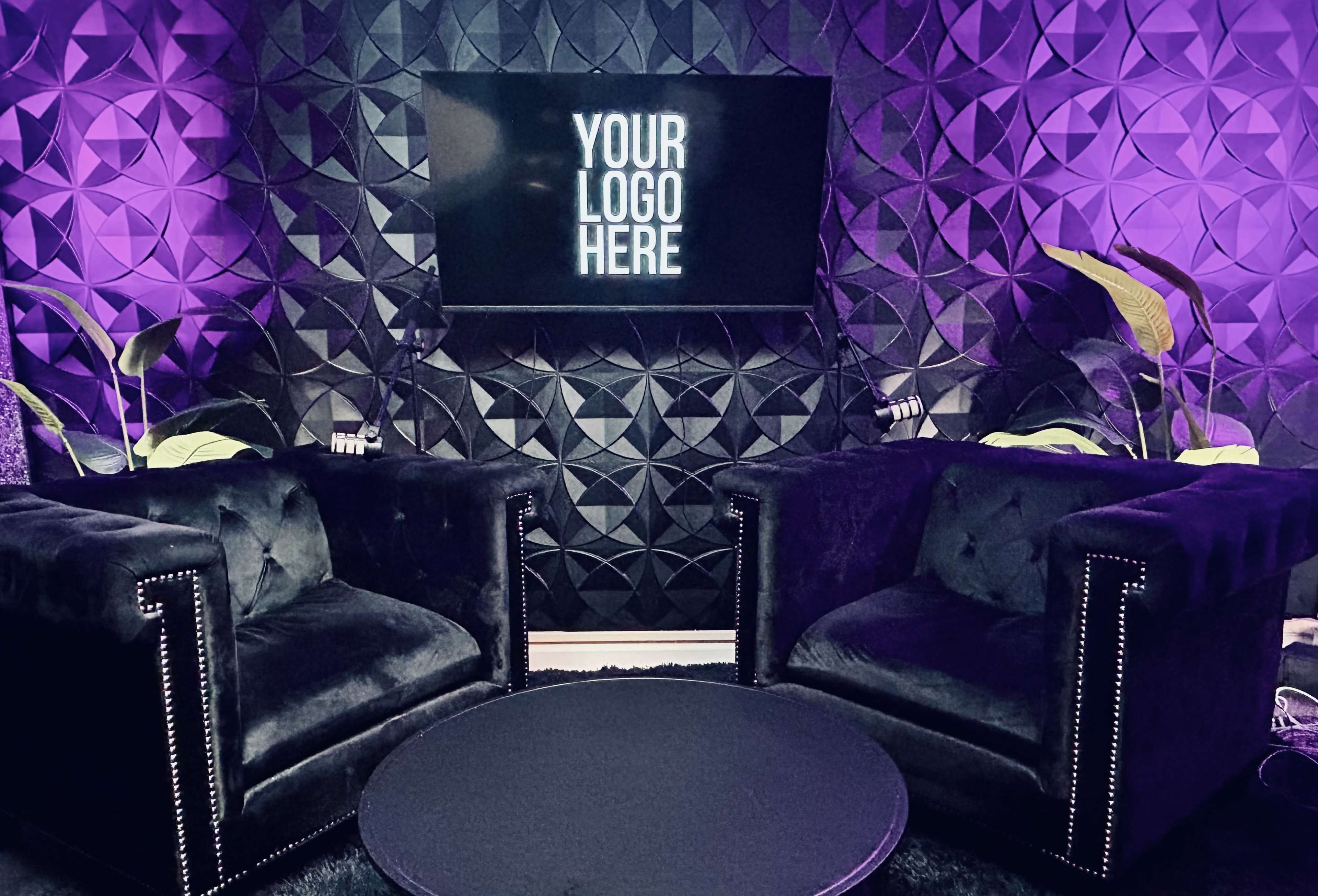 The image shows a modern seating area with two black velvet armchairs and a round table, set against a textured wall featuring purple lighting and a television displaying the text "YOUR LOGO HERE."