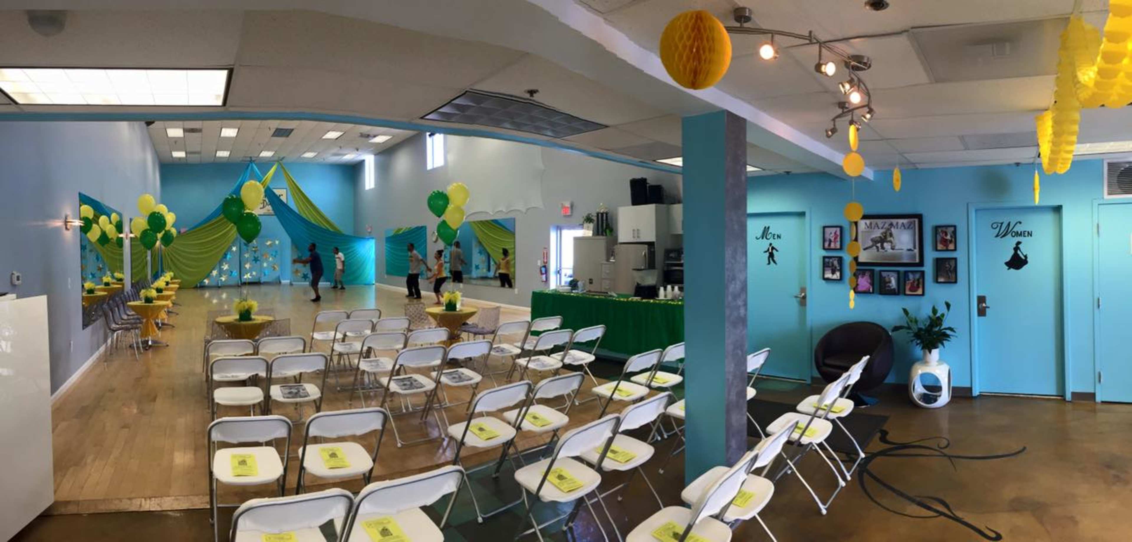 A decorated event space with green and yellow decorations, folding chairs arranged for guests, and a serving area in the background.