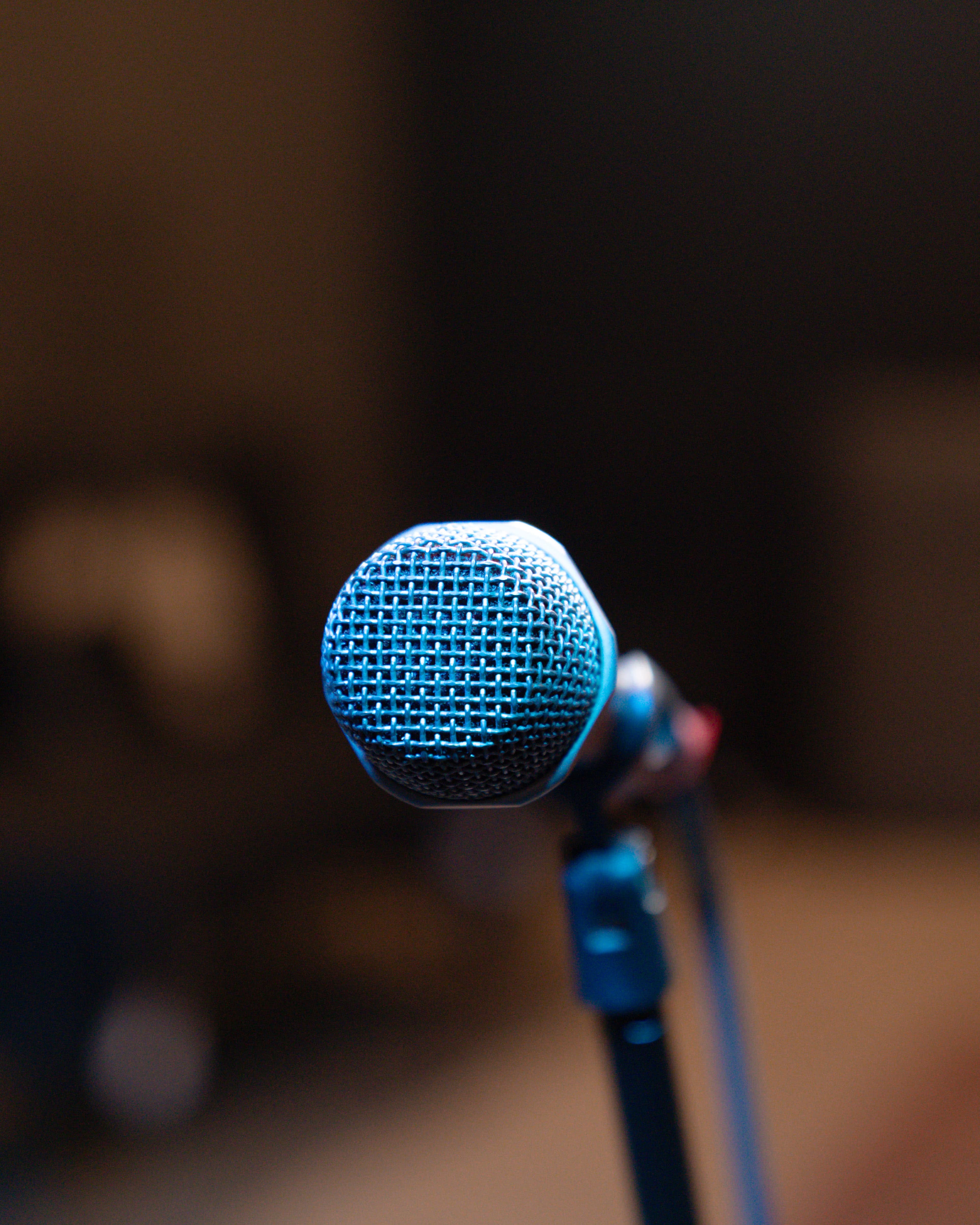 A close-up of a blue microphone on a stand is shown against a blurred background.