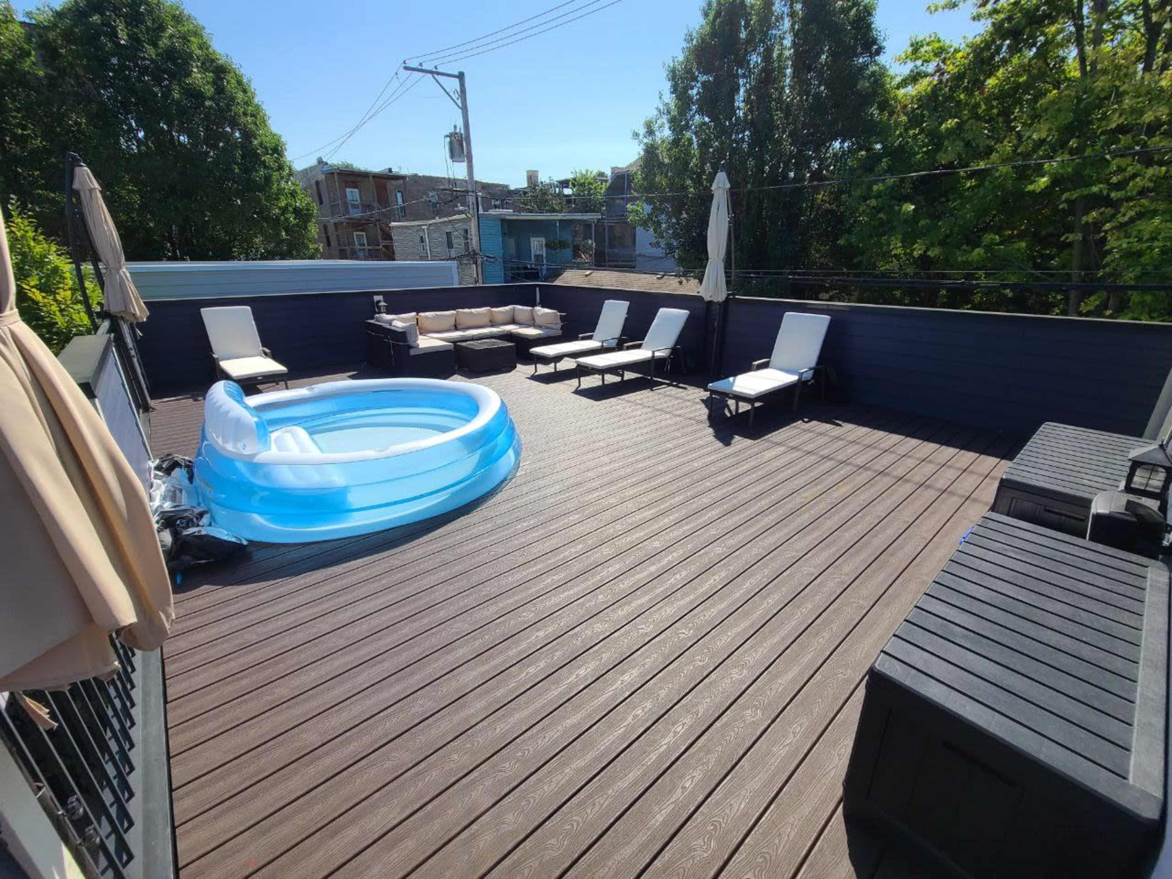 A rooftop deck featuring an inflatable pool, several lounge chairs, and patio furniture under clear blue skies.