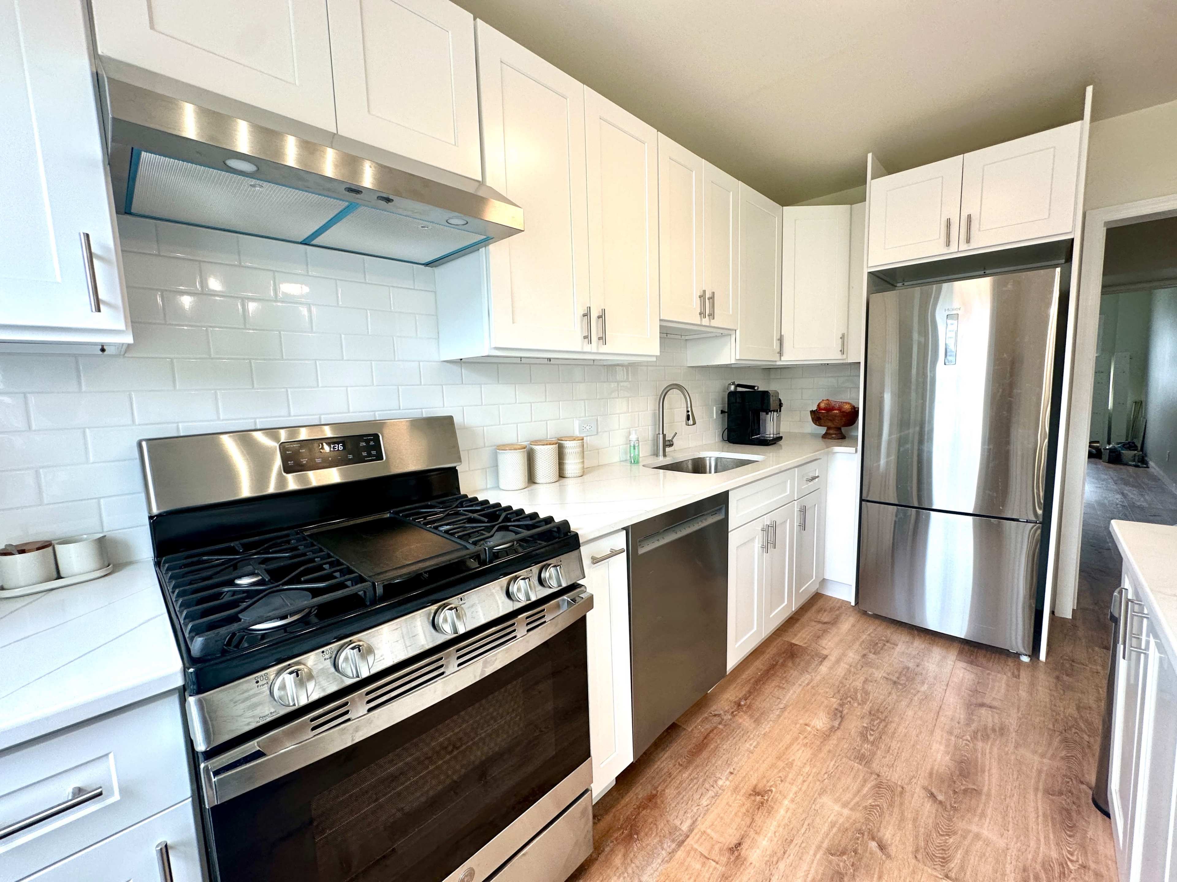 The image shows a modern kitchen with white cabinetry, a stainless steel gas stove, and a refrigerator, along with a sink and countertop.