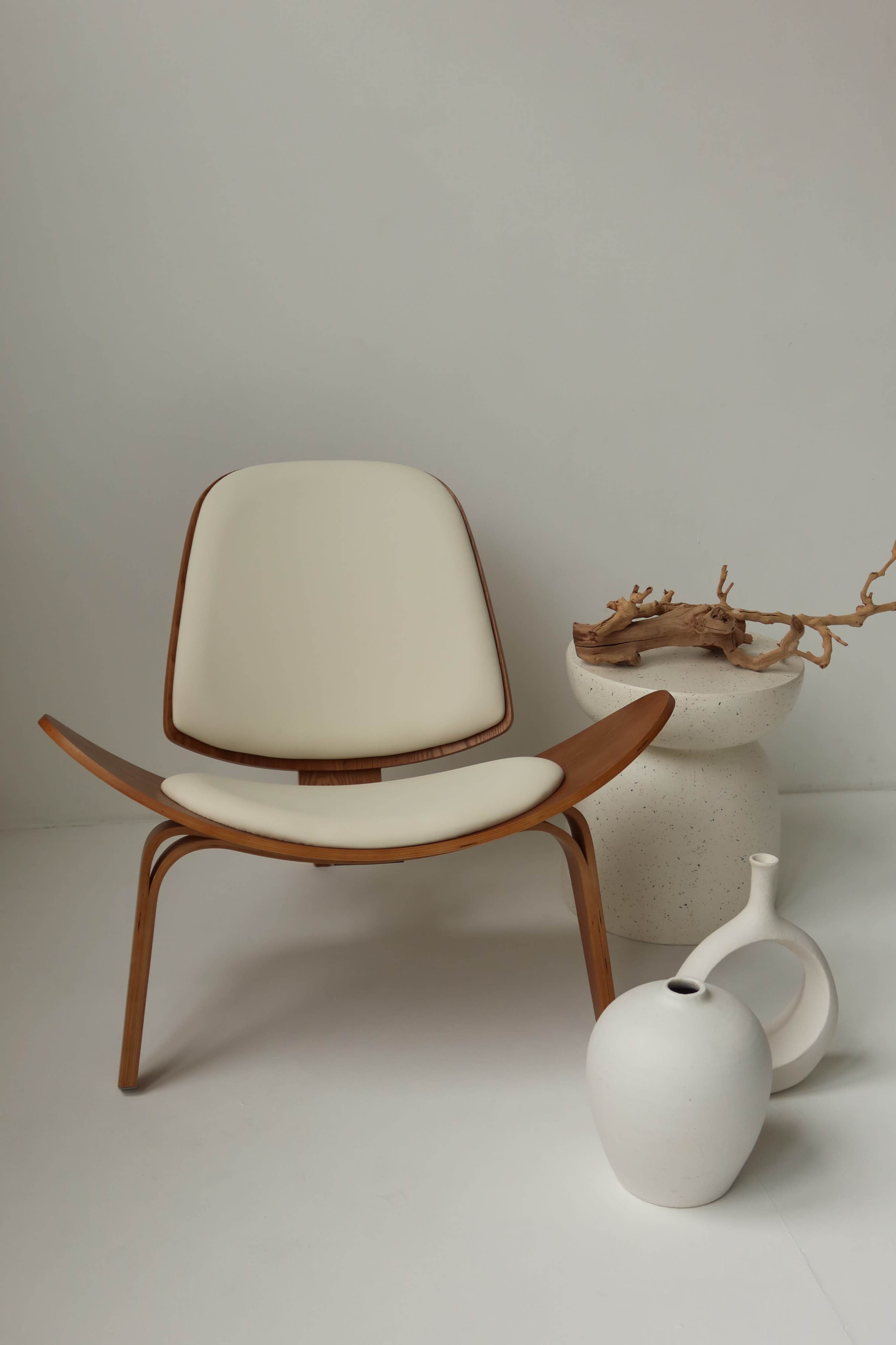 The image shows a minimalist room featuring a modern chair, a round textured vase, and a white ceramic pitcher arranged on a plain background.