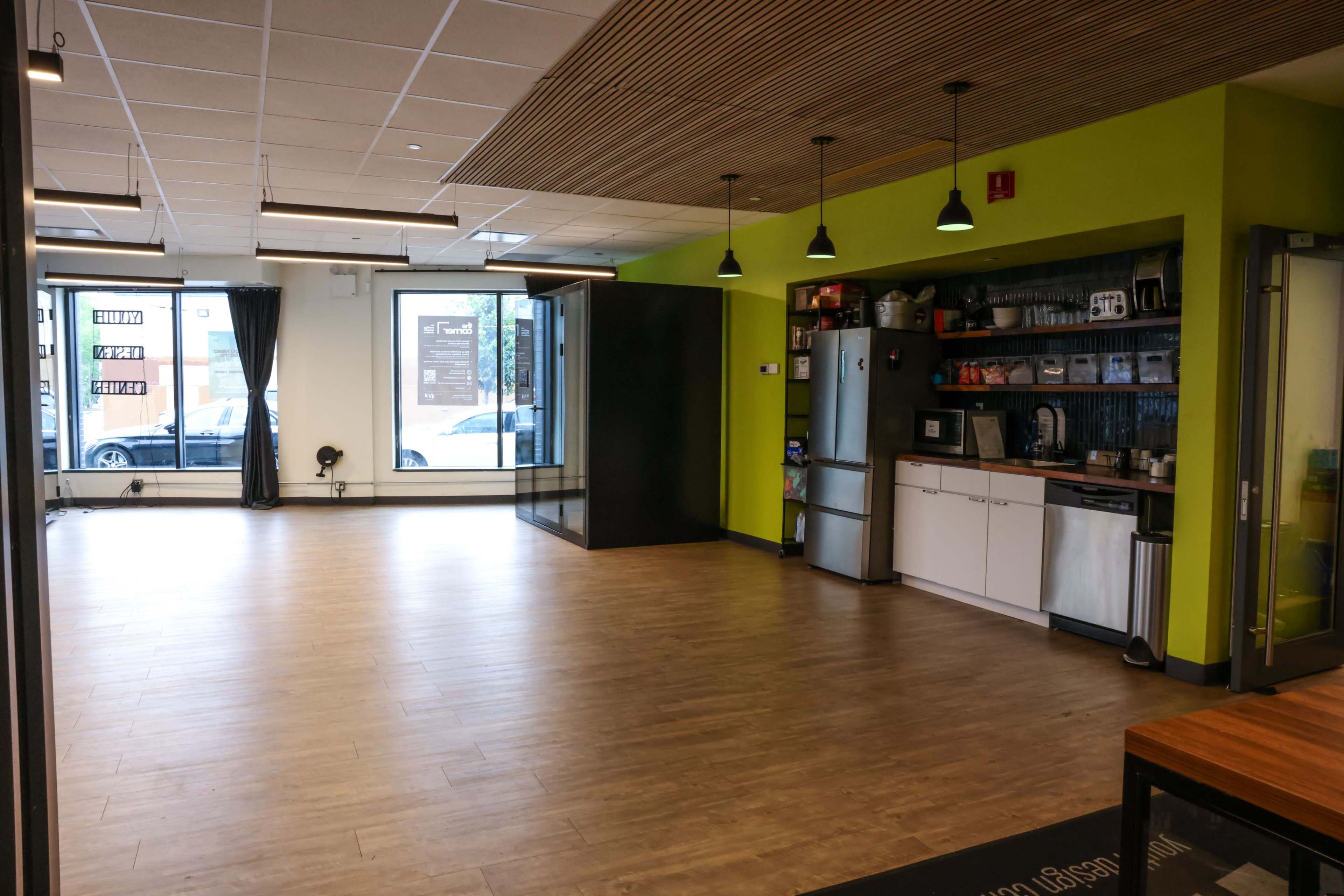 The image shows an empty interior space with hardwood flooring, green walls, and a kitchenette in one corner.