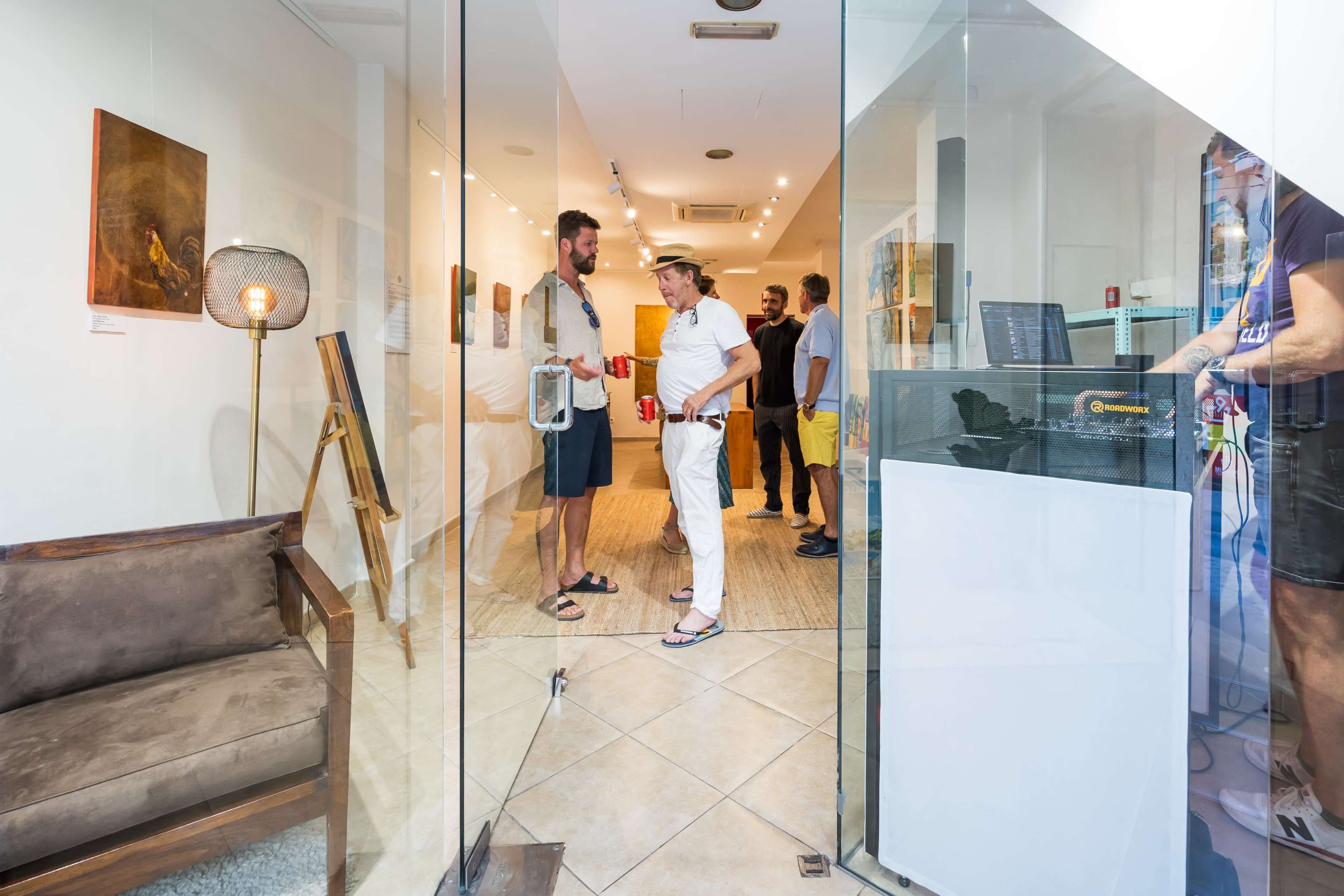 Two men converse in an art gallery while another person and a woman observe the artwork nearby.