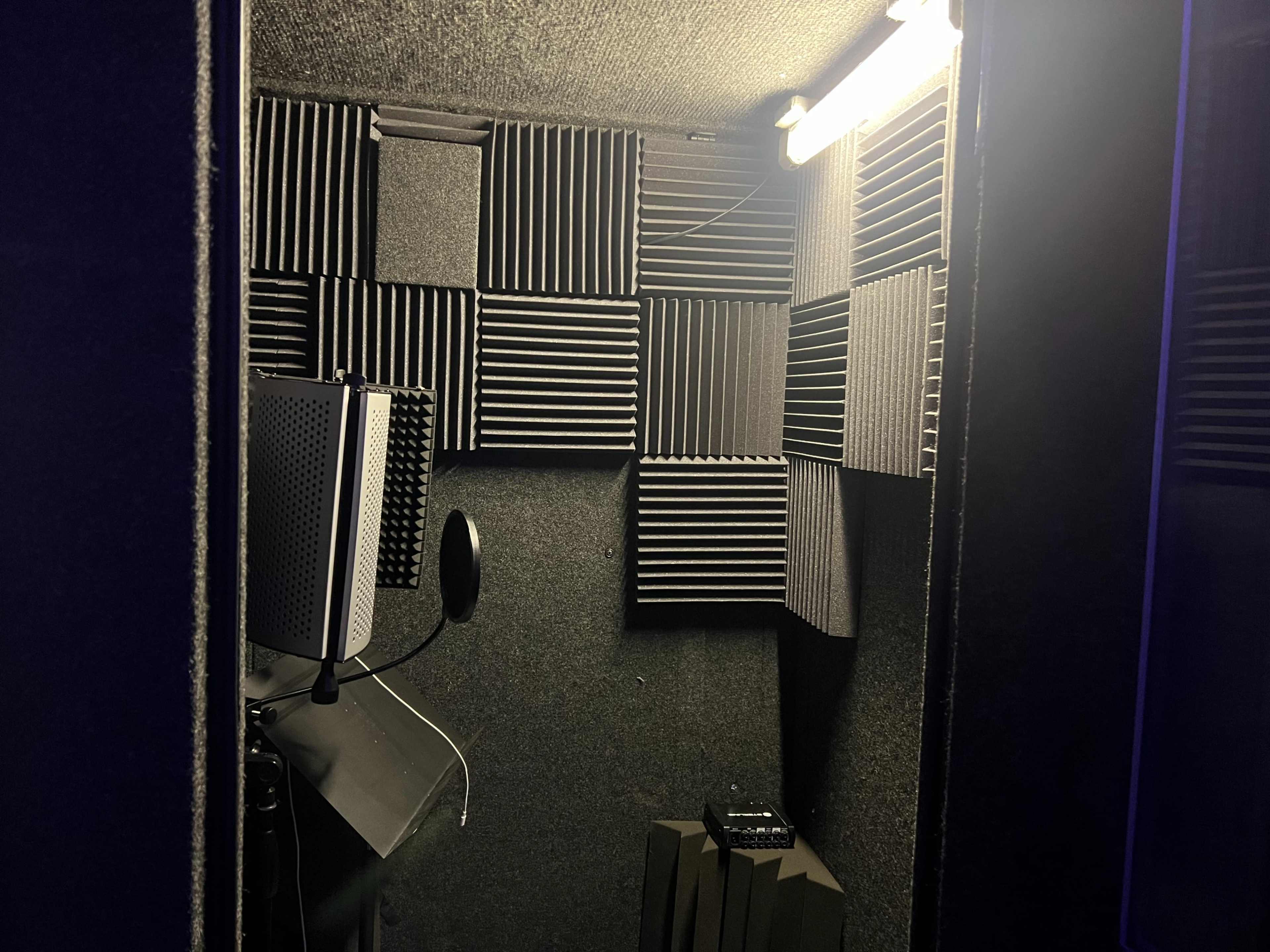 A soundproof recording booth with foam acoustic panels lining the walls and a microphone setup.