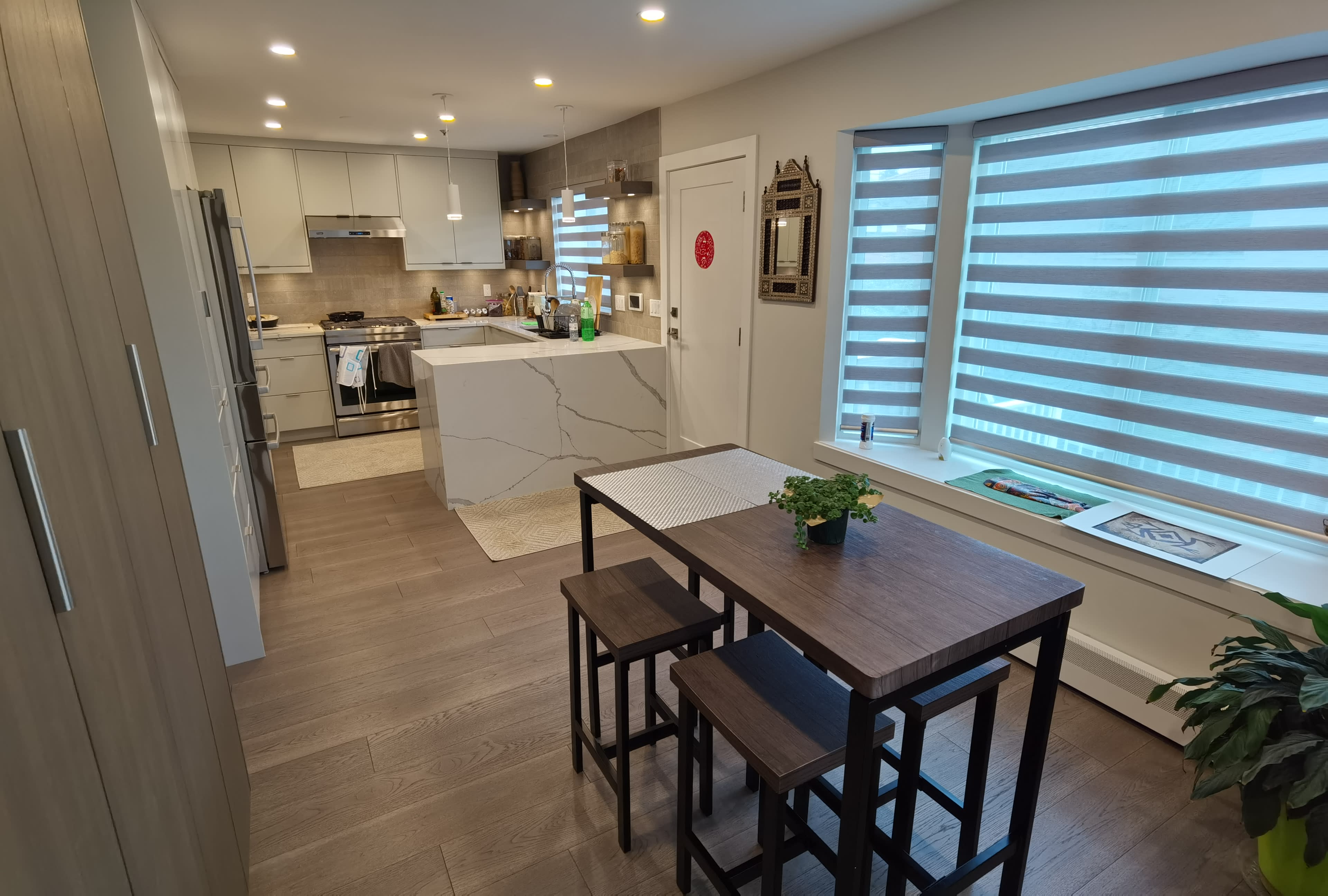 A modern kitchen and dining area with a small table and two chairs, featuring sleek cabinets and a large island counter.