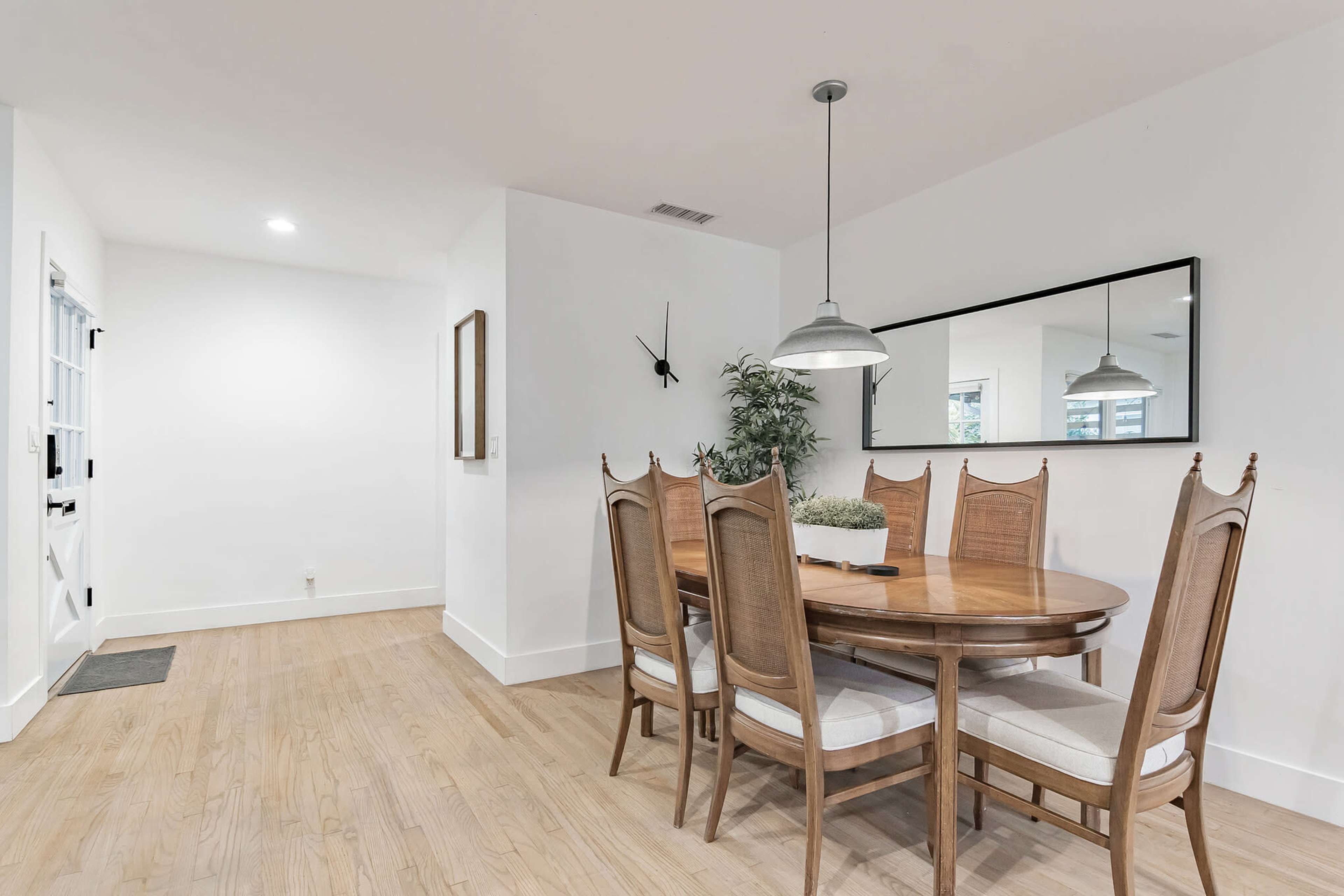 A wooden dining table with eight chairs is set against a white wall in a bright, minimalist dining area.