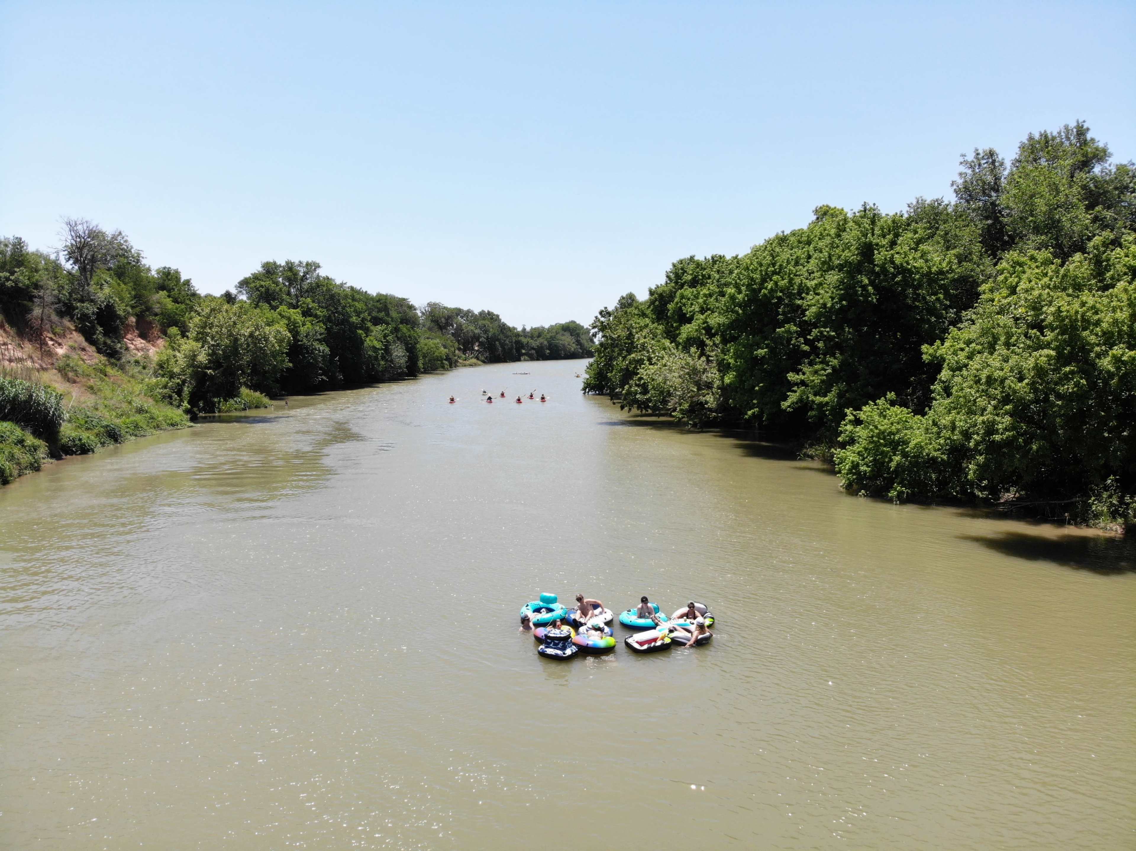 A group of people are floating on large inflatables in a river surrounded by lush green trees.