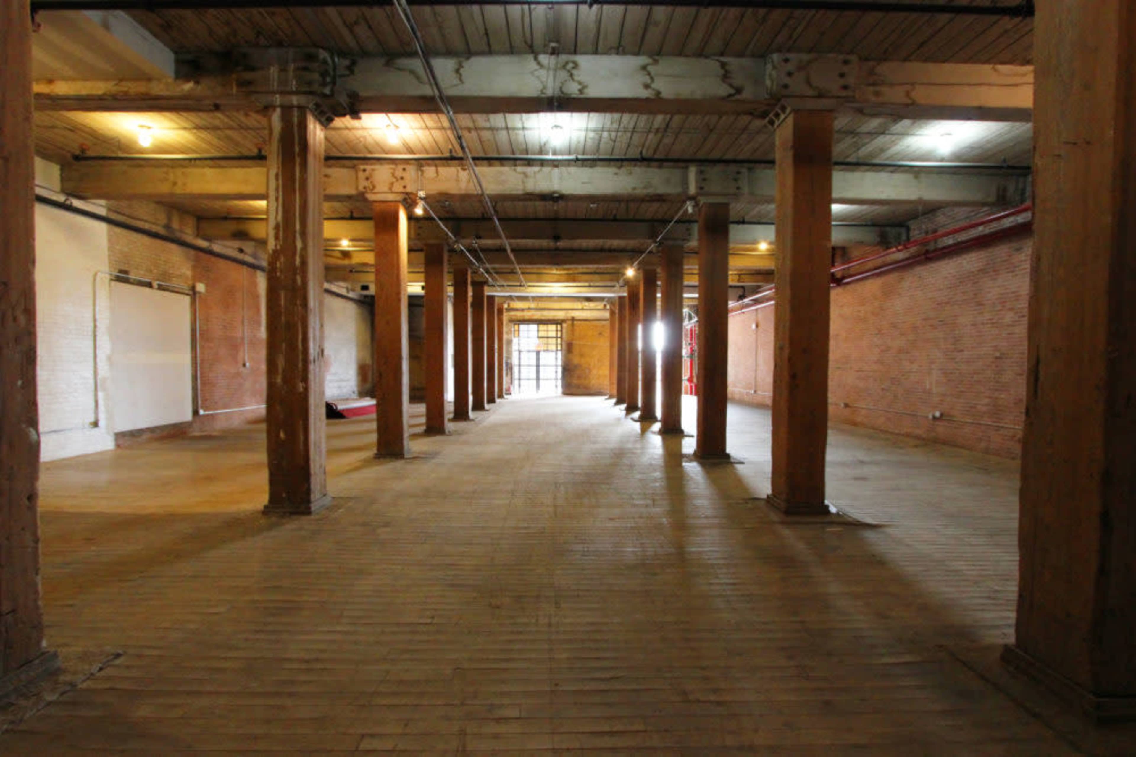 An empty industrial space featuring wooden floors and multiple supporting pillars.