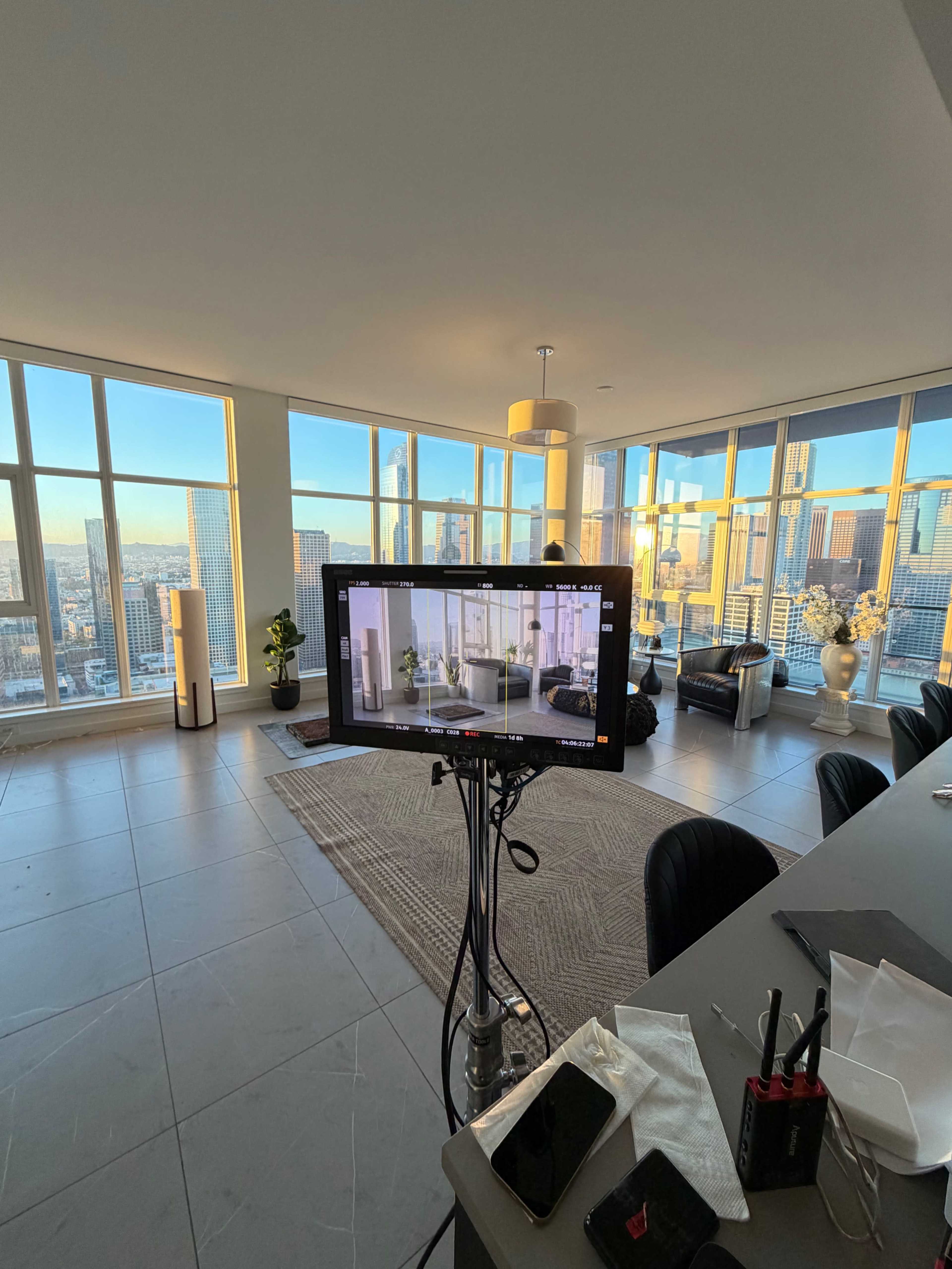 A camera monitor displays a view of an elegantly furnished room with large windows overlooking a city skyline.