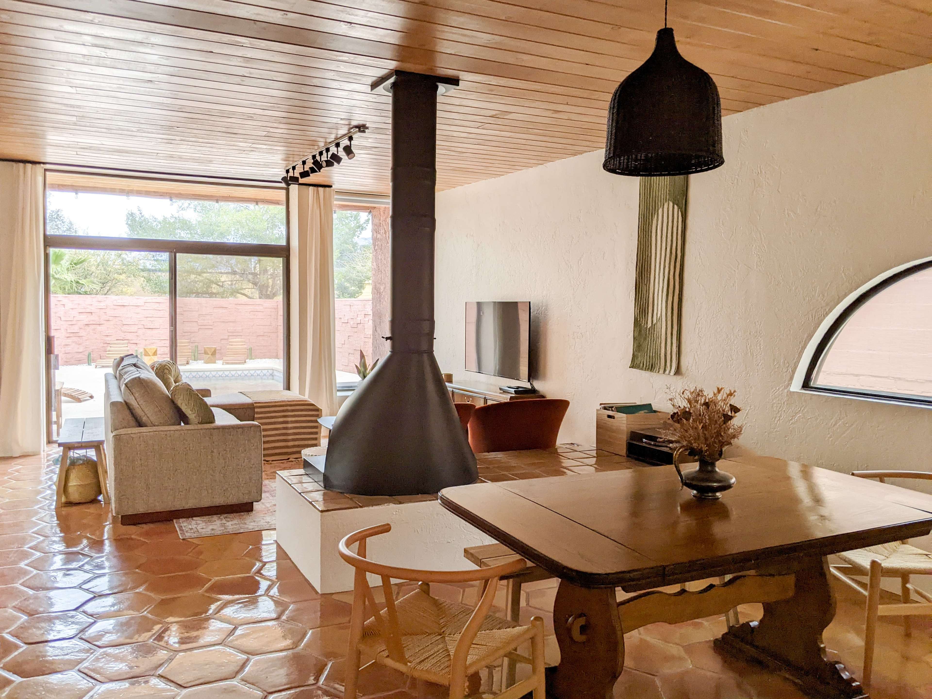 A spacious, modern living area with a dining table, a wood-burning stove, a television, and large windows that open to an outdoor space.