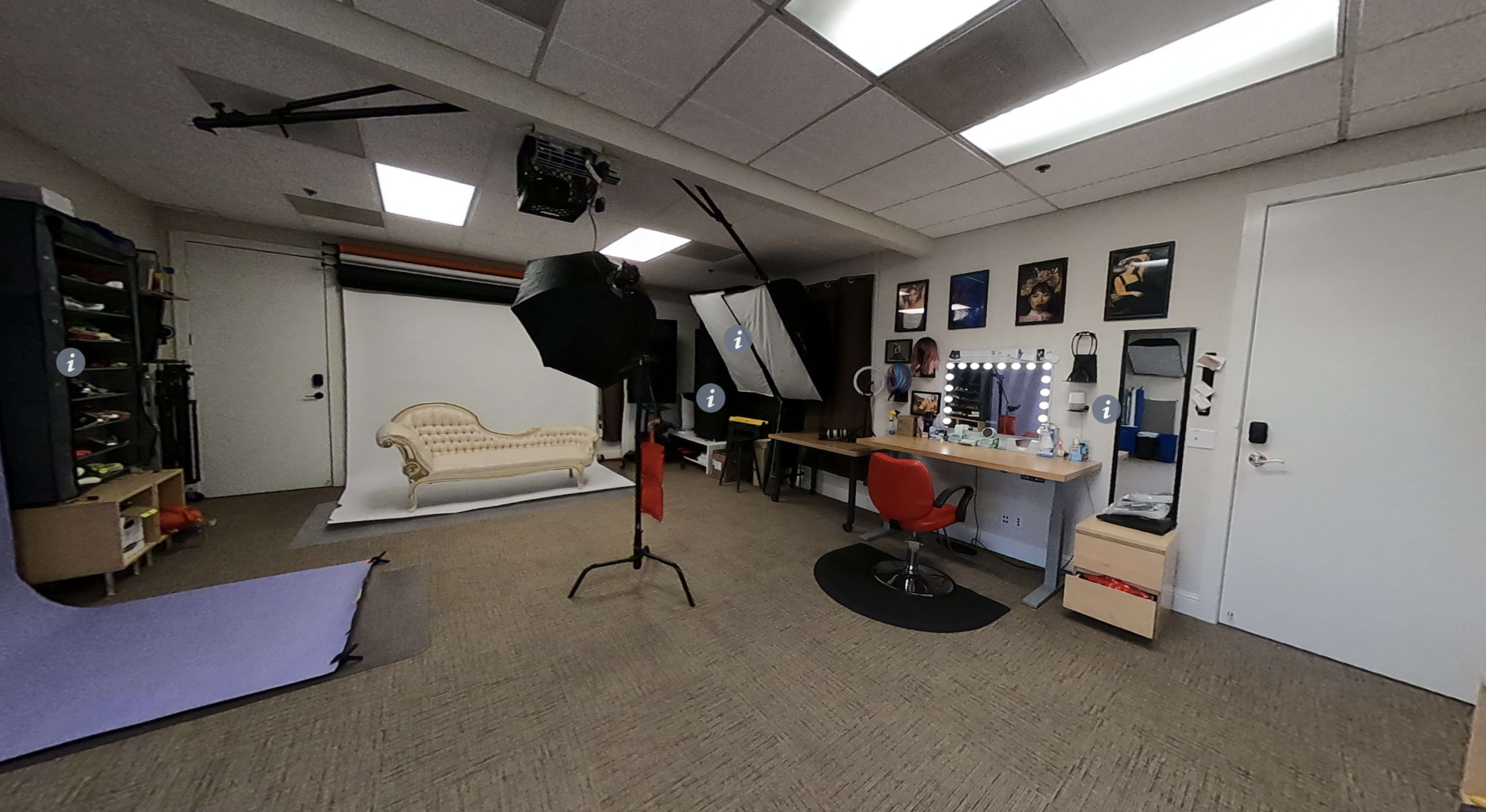 A photography studio featuring a vintage sofa, a makeup station with a mirror, and various lighting equipment.