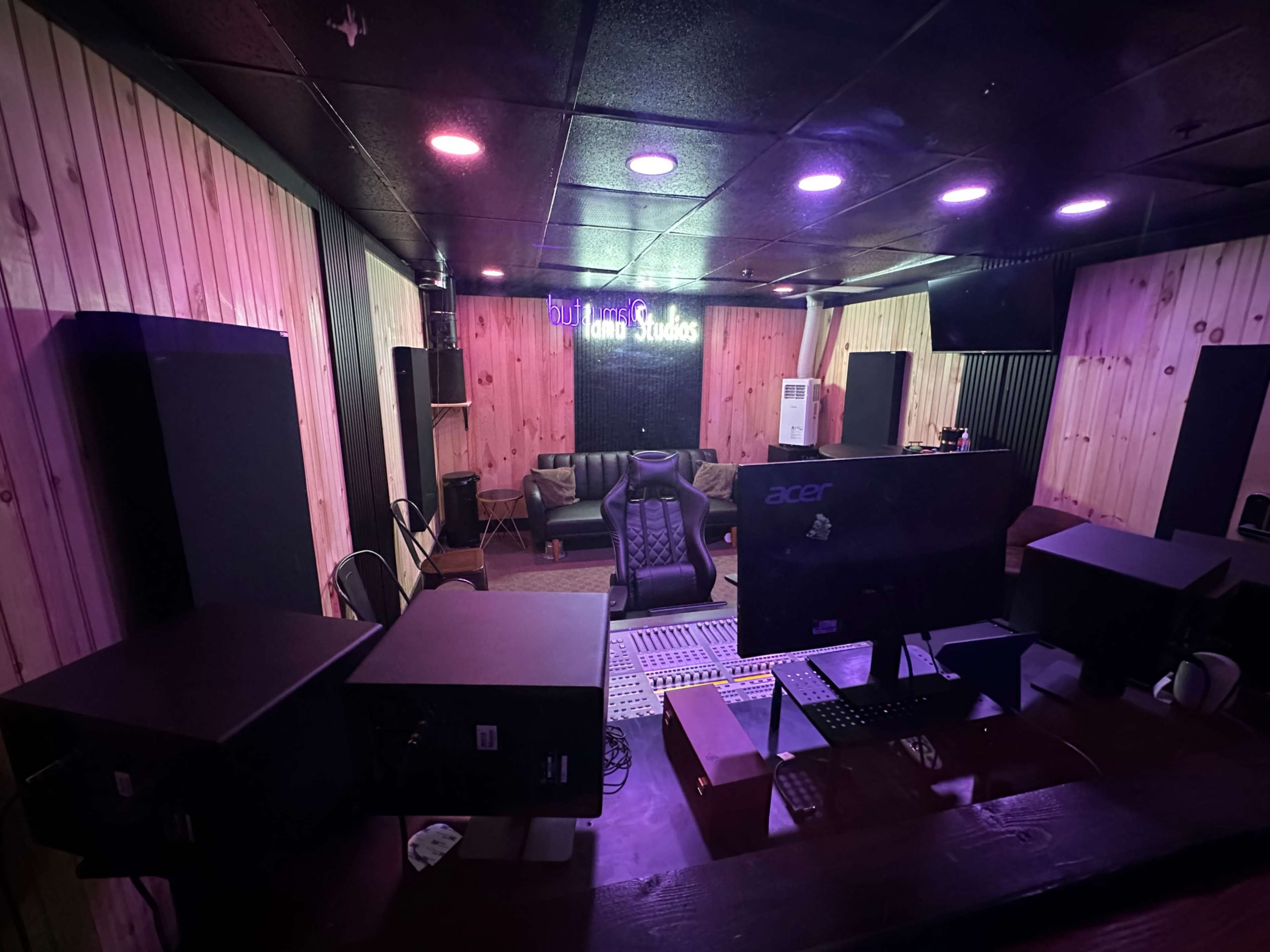 A recording studio with wooden walls, a mixing console, and a sofa.