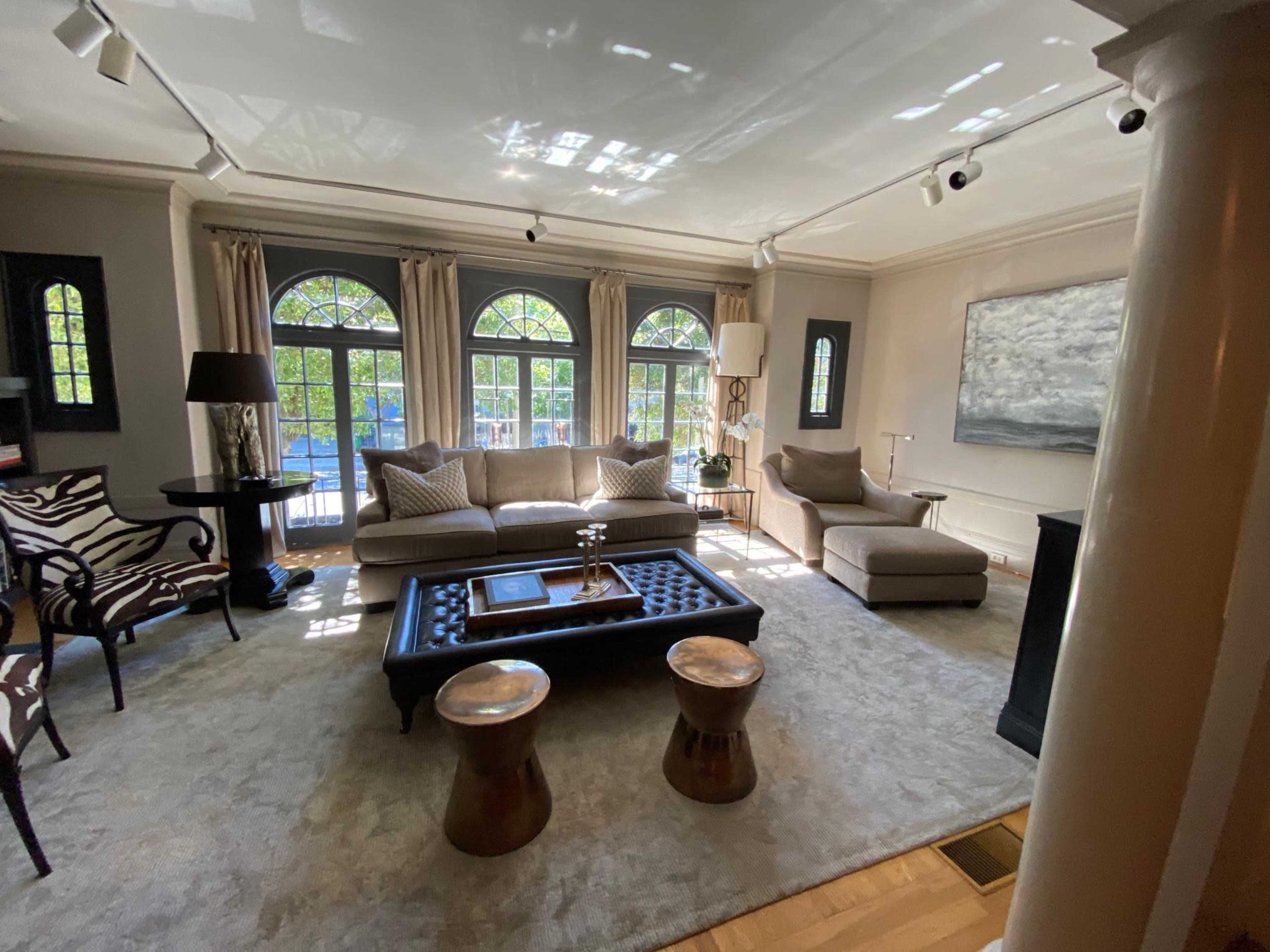 The image shows a well-furnished living room featuring large arched windows, a plush sofa, a coffee table, and decorative side tables.