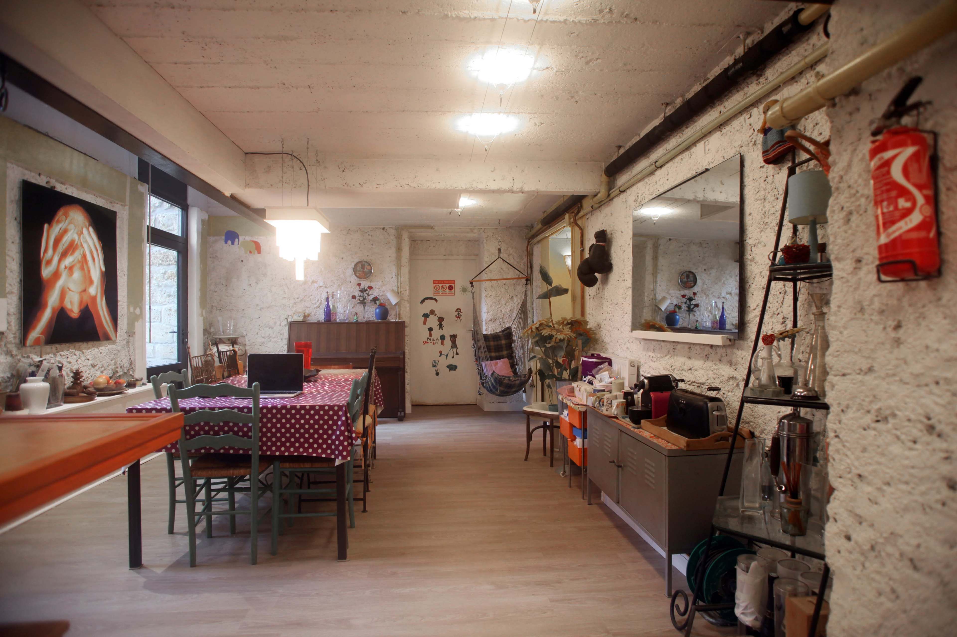 The image shows an interior of a spacious room with a dining table, chairs, and various decorative items against a textured wall.
