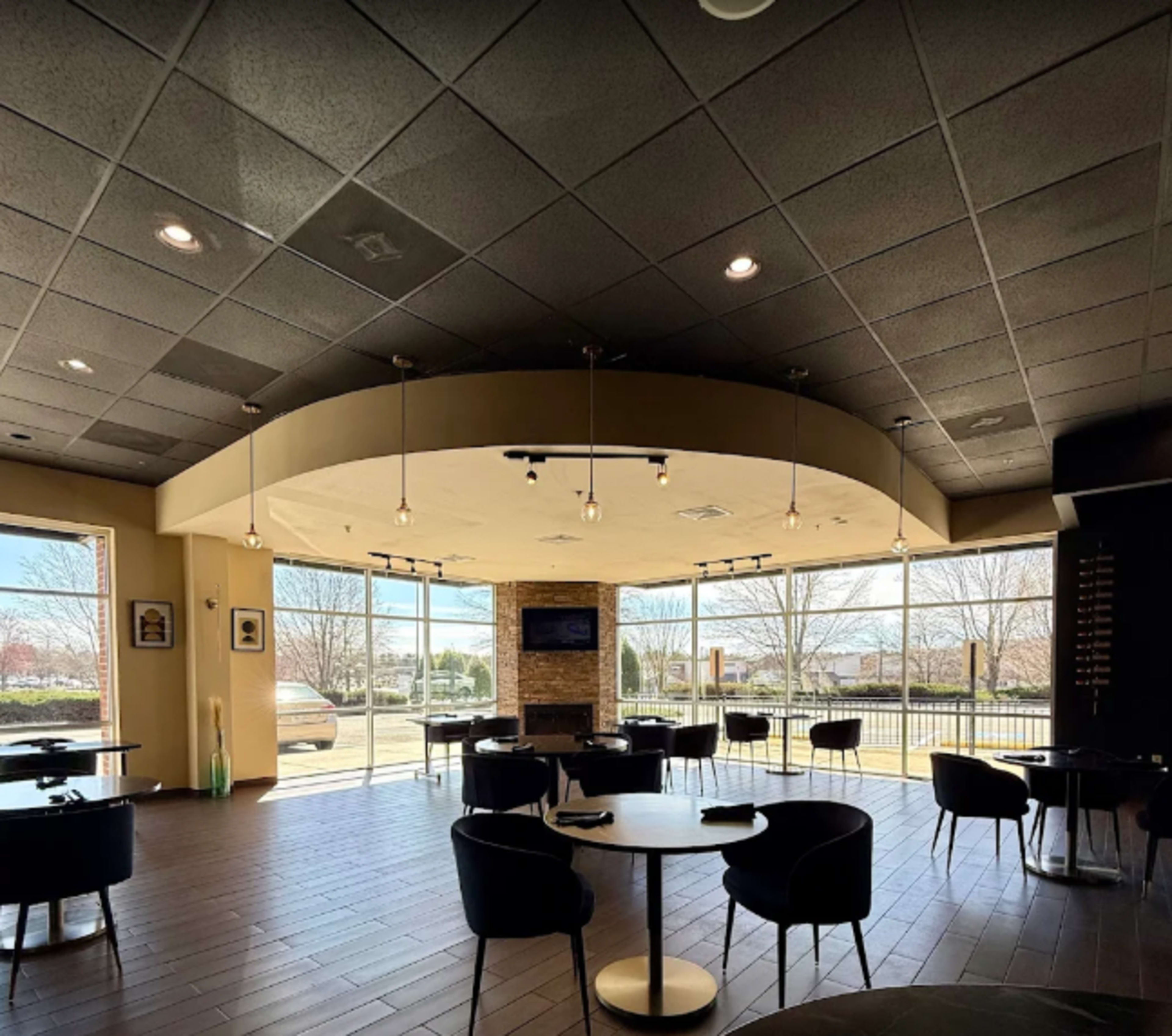 The image shows a modern café interior with large windows, round tables, and a central fireplace area.