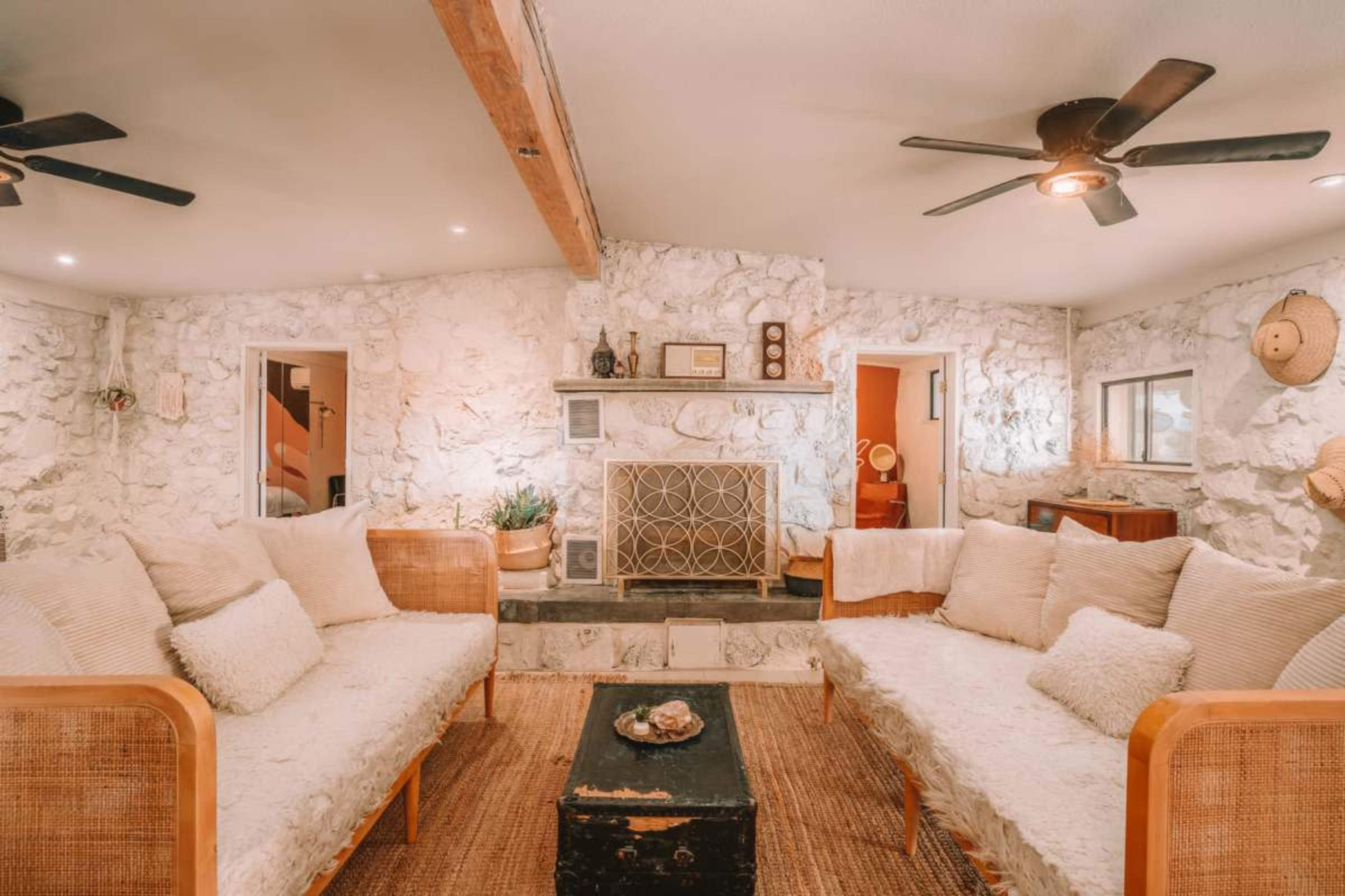 The image shows a cozy living room with stone walls, two rattan sofas facing a central coffee table, and a fireplace in the background.